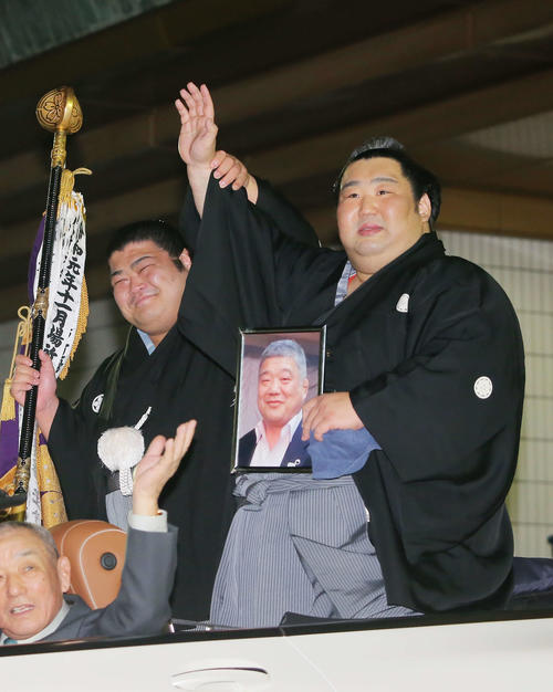 亡き恩師の近大相撲部伊東監督の遺影を手に、優勝パレード車から笑顔で手を振る徳勝龍(右)と旗持ちの志摩ノ海(撮影・河田真司)