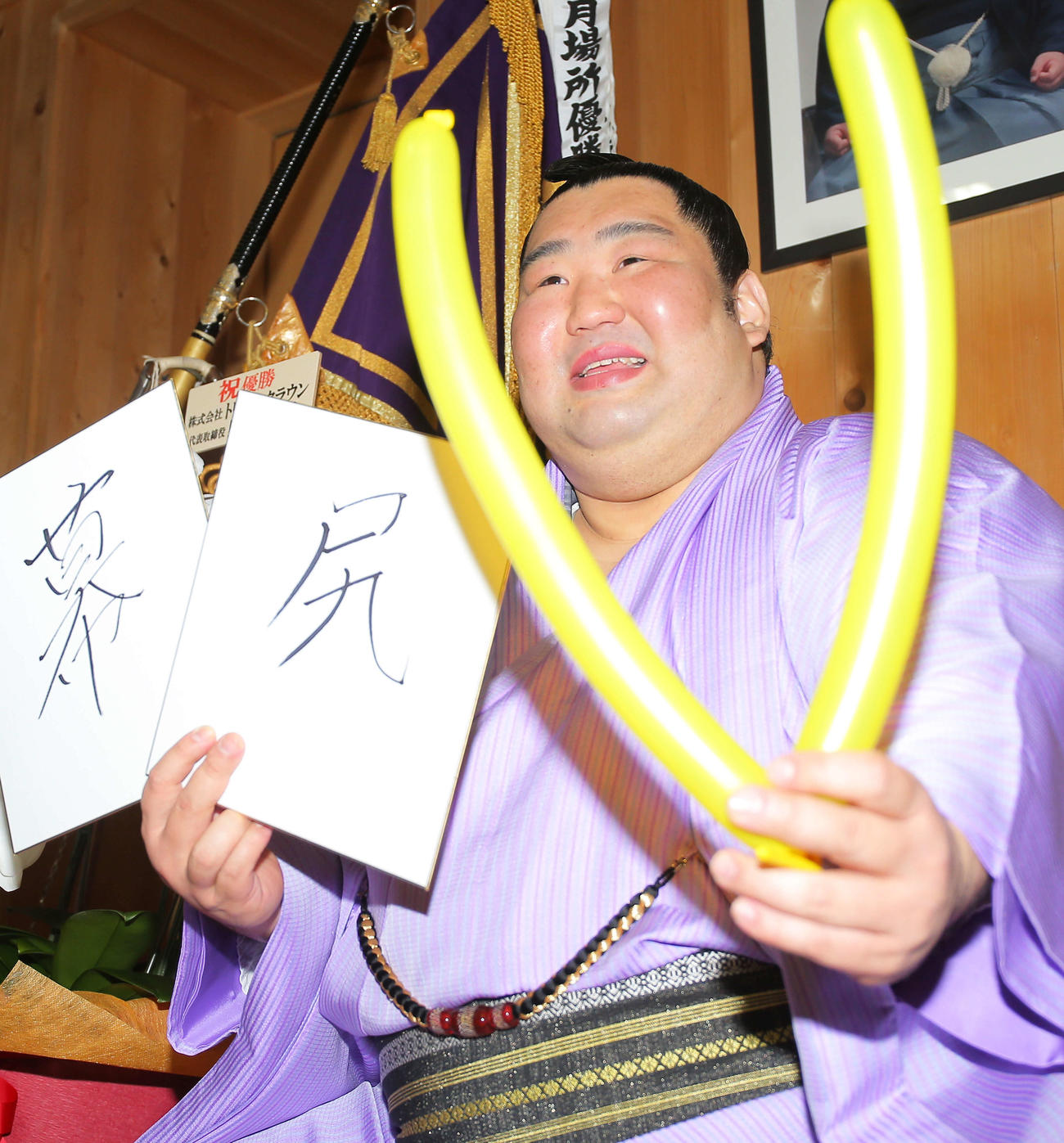 幕内優勝を飾り、一夜明け会見で「幕尻」としたためた色紙と、優勝の「V」バルーンを手に笑顔を見せる徳勝龍（撮影・河田真司）