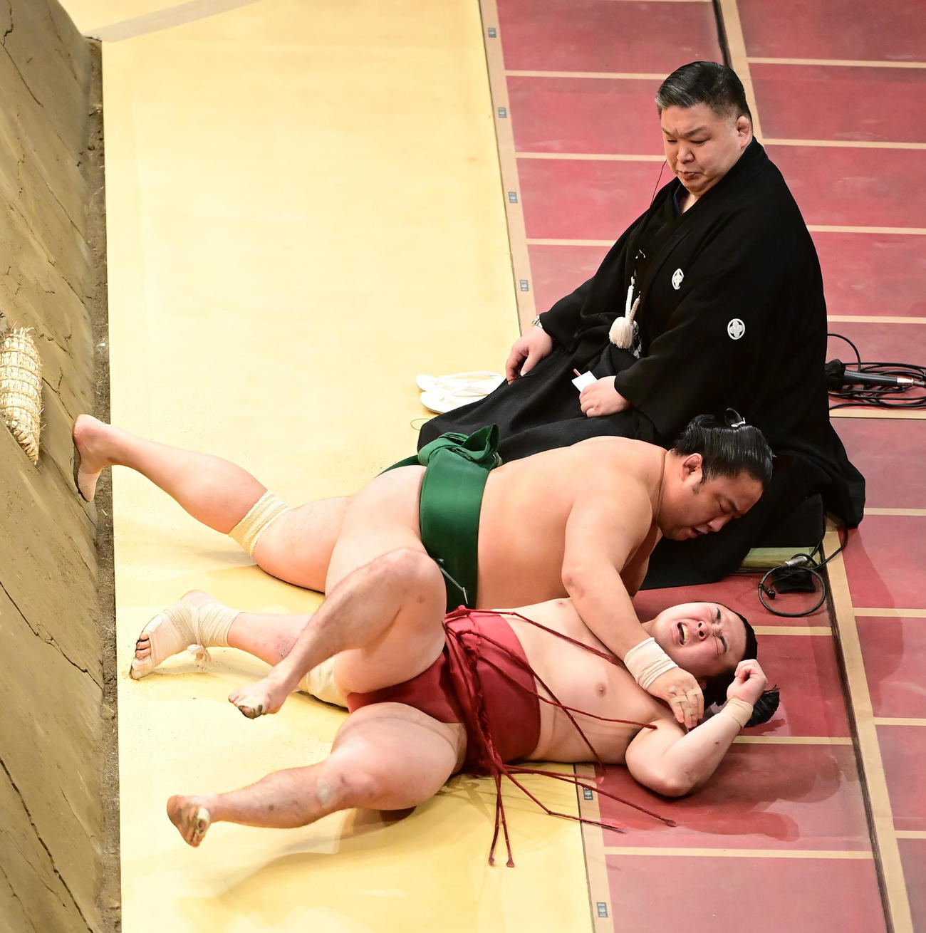 佐田の海に寄り切りで敗れた炎鵬（手前）はそのまま土俵下に落ち痛そうな表情を見せる。奥は高田川審判長（撮影・小沢裕）