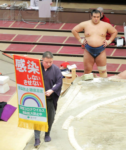 玉鷲を引き落としで破った千代の国は、土俵上を回る新型コロナウイルス感染拡大防止を呼びかける懸賞旗スタイルの告知旗を見つめるながら土俵下で待機する（撮影・河田真司）