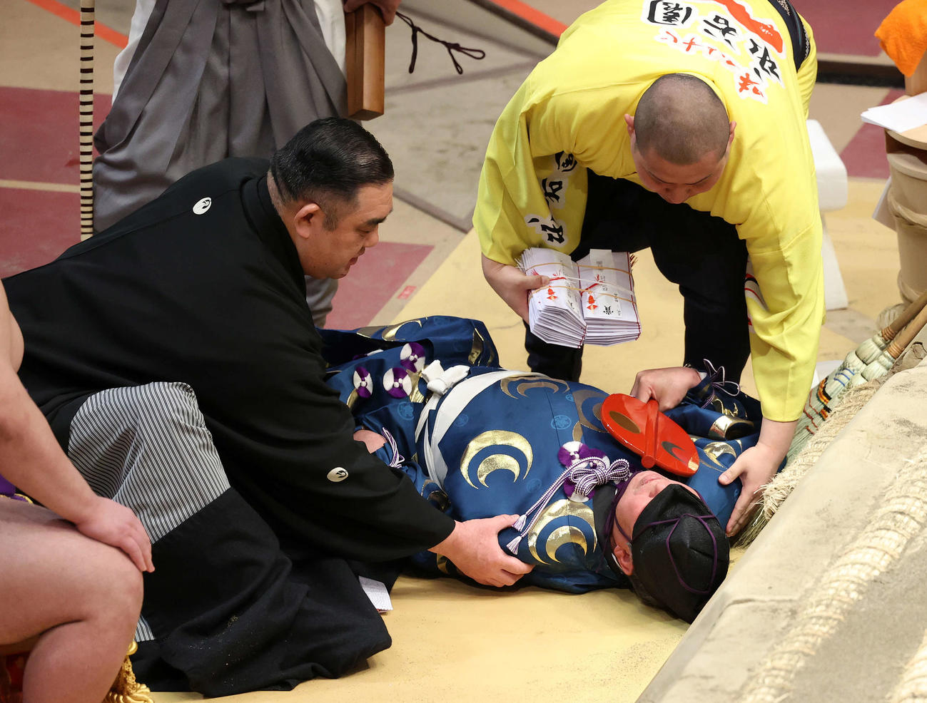 結びの一番で土俵下に落ちた立て行司の式守伊之助（中央）。声をかける西岩親方（左）と呼び出し（撮影・鈴木正人）