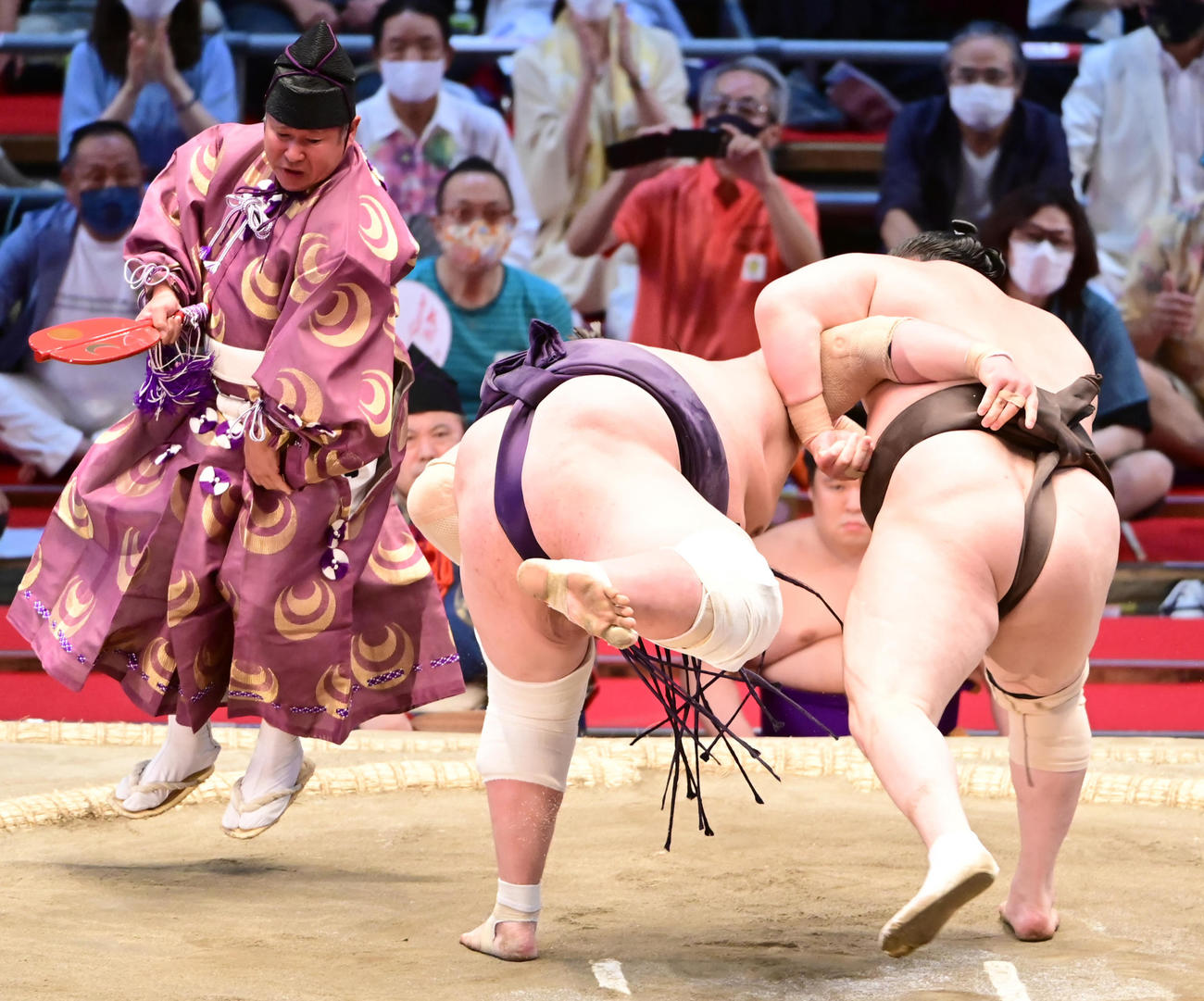 白鵬（右）に投げを打たれ体勢を崩した照ノ富士を避けて飛び上がる行司の式守伊之助（撮影・小沢裕）