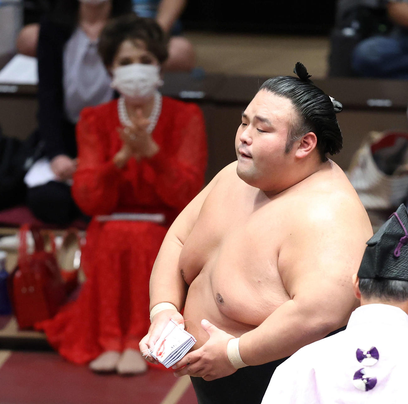 豊昇龍突き落としで破り、懸賞金の束を手に土俵から引き揚げる貴景勝。後方左は拍手するデヴィ夫人（撮影・河田真司）