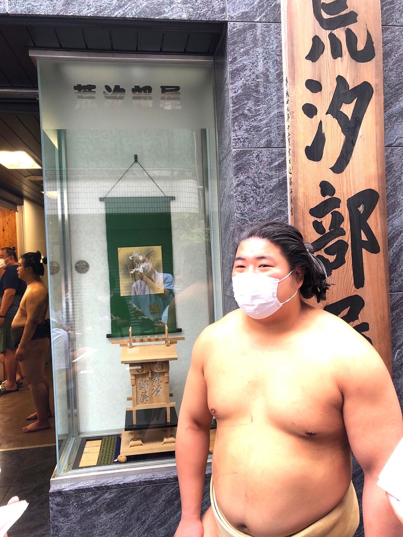 部屋の看板の前で取材に応じる若元春