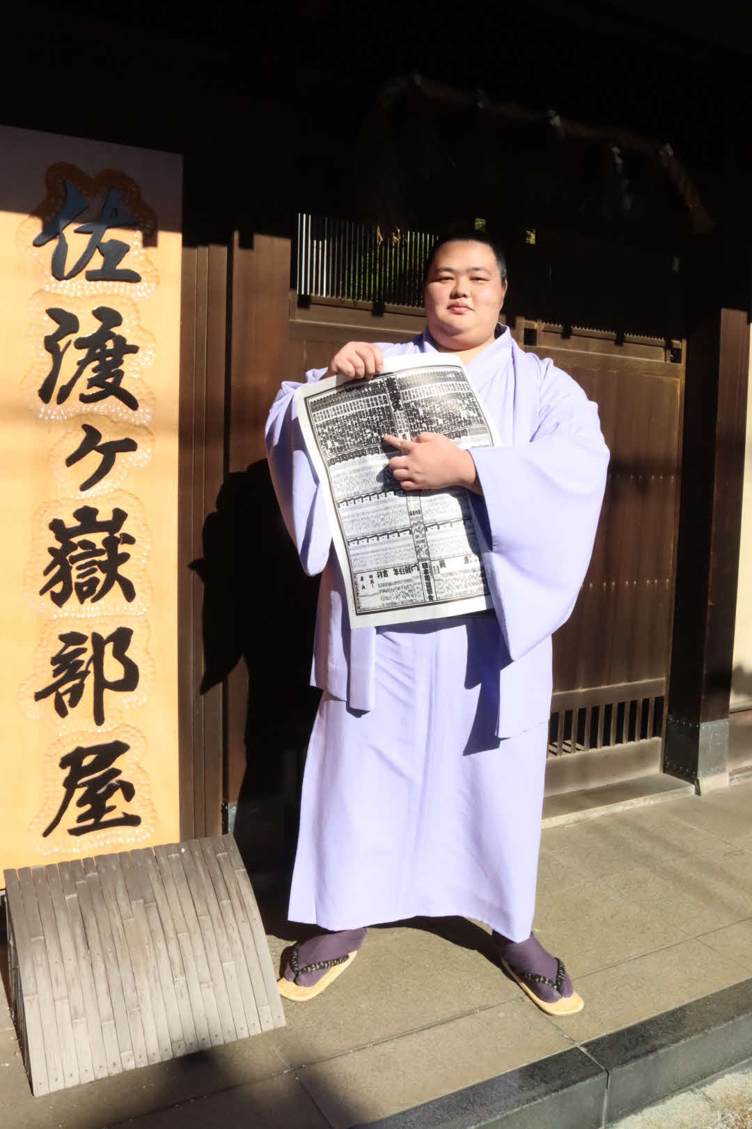 佐渡ケ嶽部屋の前で来年1月の大相撲初場所の番付表を持つ新小結の琴ノ若（日本相撲協会提供）