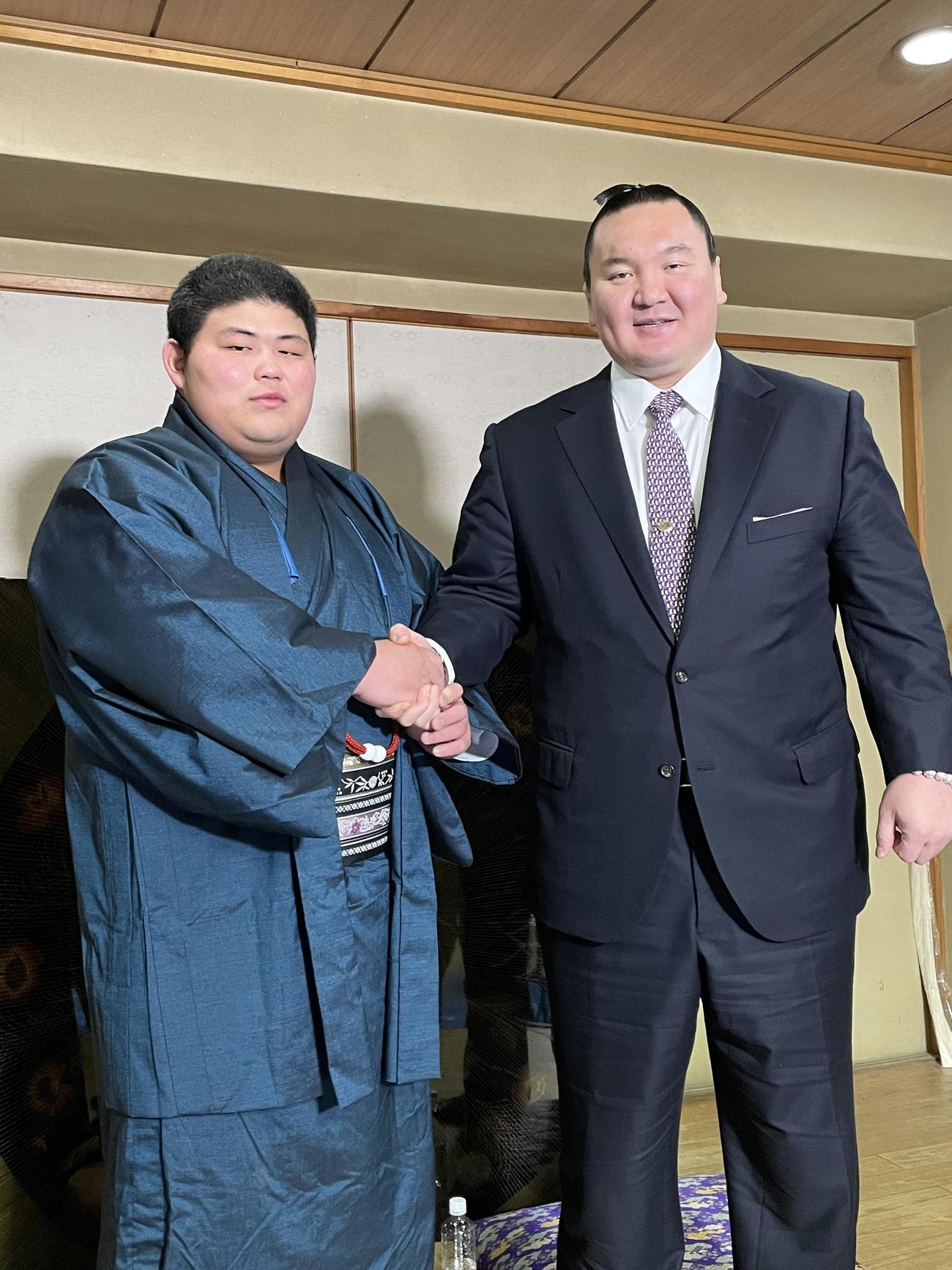 新十両会見で握手を交わす落合（左）と宮城野親方（日本相撲協会提供）