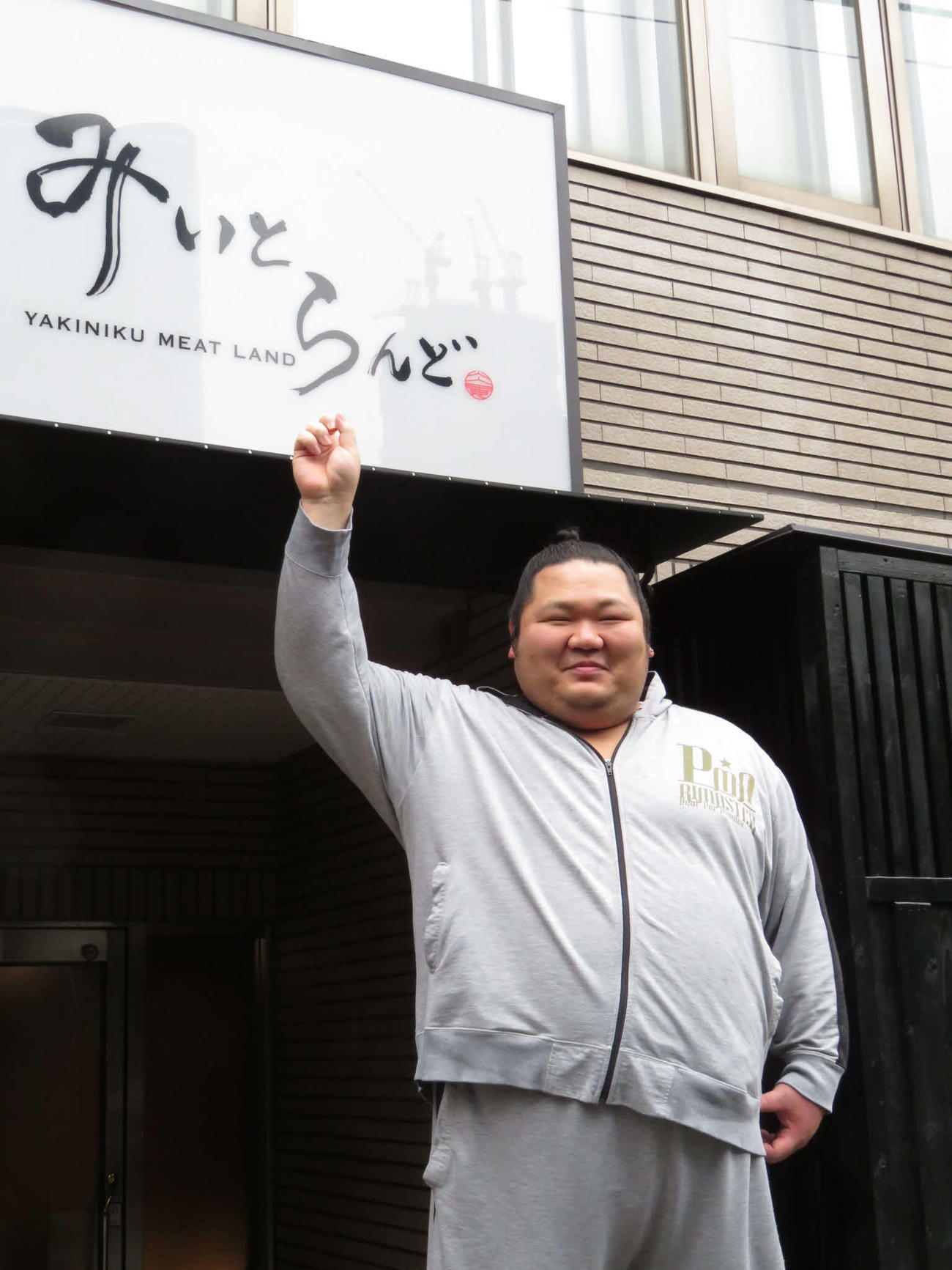 東京・六本木にオープンさせた焼き肉店「みいとらんど」の看板を指さし、笑顔を見せる元小結千代大龍の明月院秀政さん