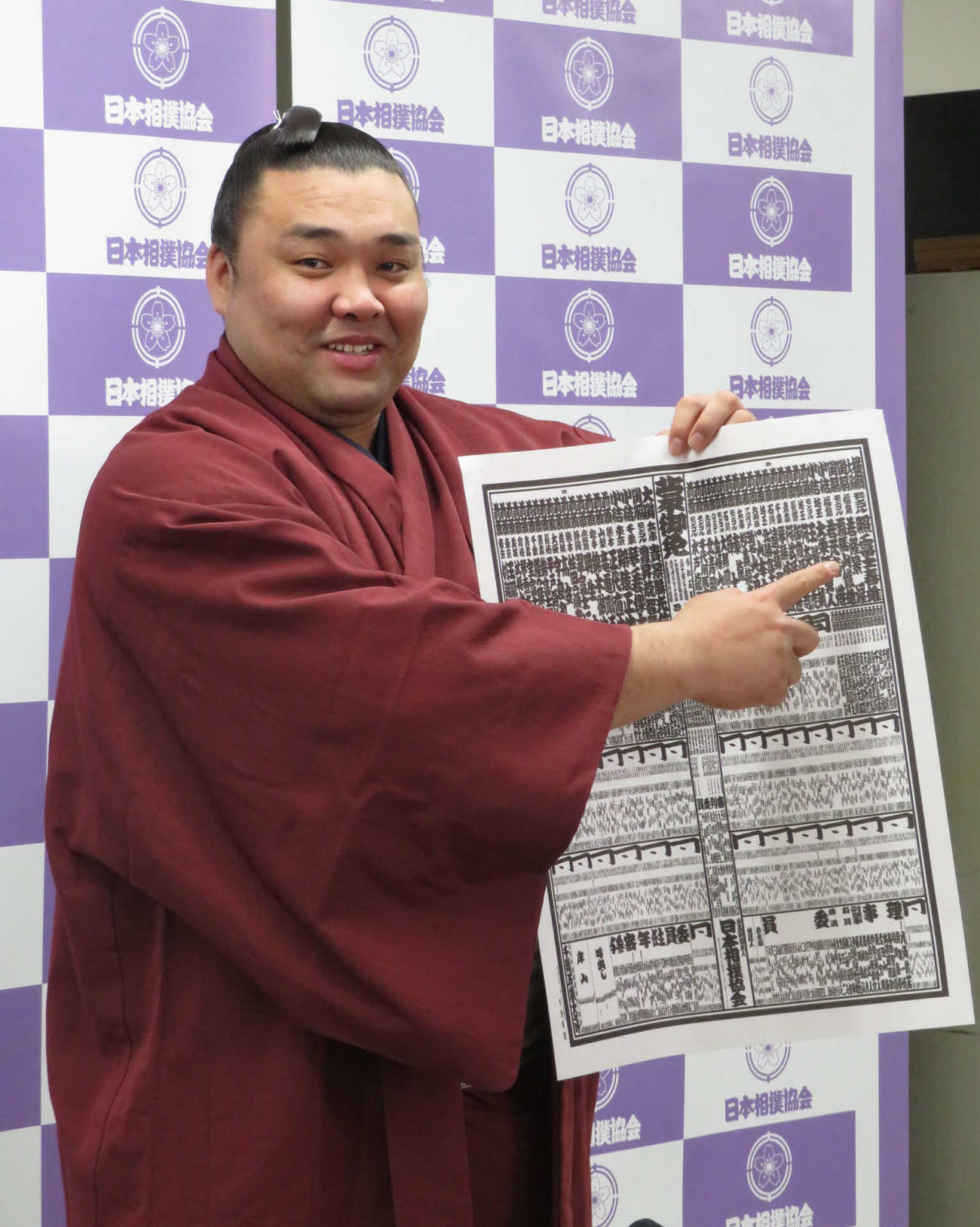 新関脇に昇進し、自身のしこ名を指さして笑顔を見せる霧馬山