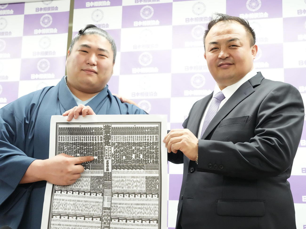 大相撲夏場所の番付発表会見で自らの名前を指し笑顔を見せる若元春。右は師匠の荒汐親方（撮影・小沢裕）