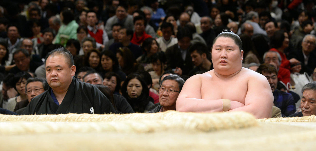 2015年1月、土俵下の控えで師匠の湊親方（元湊富士＝左）の隣に座る逸ノ城