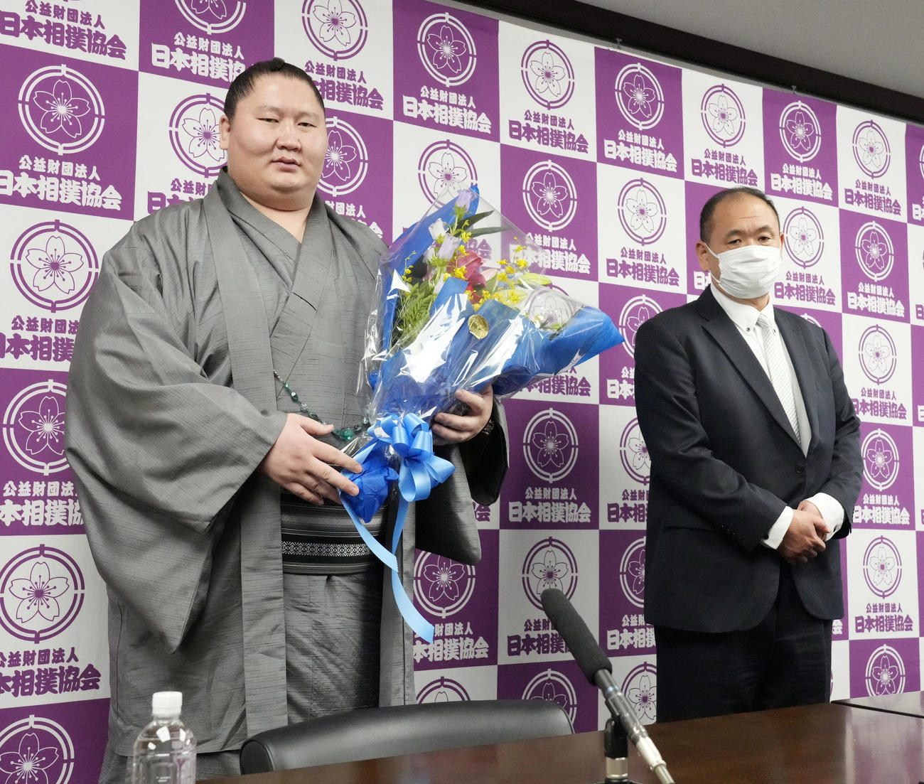 引退会見を終え報道陣から贈られた花束を手にする逸ノ城。右は師匠の湊親方（撮影・小沢裕）