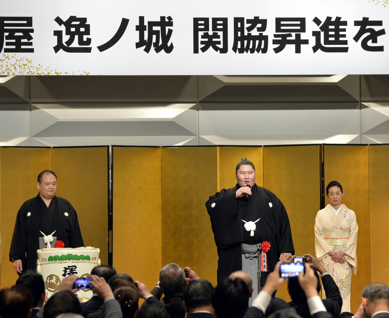 自身の関脇昇進祝賀会であいさつする逸ノ城。左は師匠の湊親方（元前頭湊富士）。右は湊親方のおかみさんの真夫人
