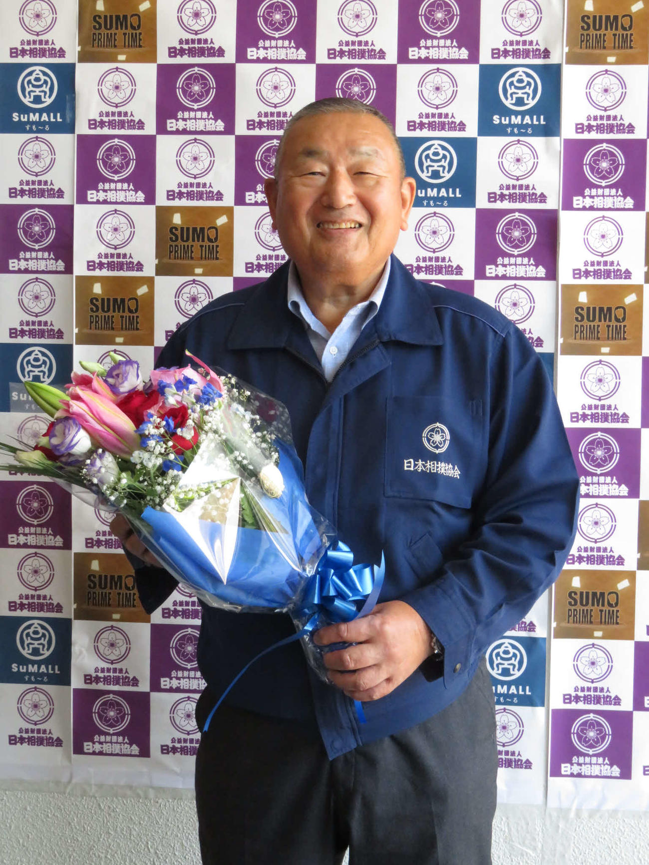 4月に定年を迎え、報道陣から贈られた花束を手に笑顔を見せる入間川親方