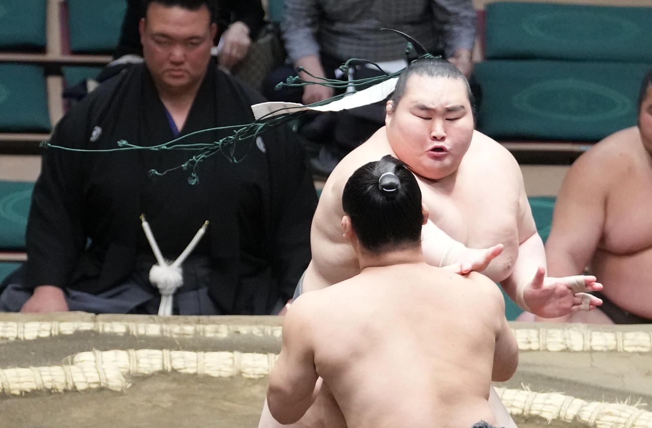 栃丸（右奥）はまわしに着用していた下がりが外れまげに絡まった状態で取組を続ける（撮影・小沢裕）