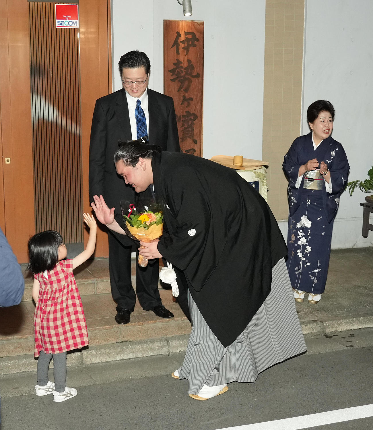 伊勢ケ浜部屋前で子供から花束贈呈を受けハイタッチする照ノ富士。後方左から師匠の伊勢ケ浜親方とおかみさんの淳子夫人（撮影・小沢裕）
