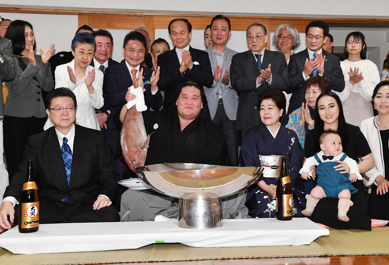 伊勢ケ浜部屋での祝賀会で、前列左から師匠の伊勢ケ浜親方、1人おいておかみさんの淳子夫人、長男・テムジン君を抱くツェグメド・ドルジハンド夫人と関係者に囲まれながらお祝いの鯛を掲げる照ノ富士