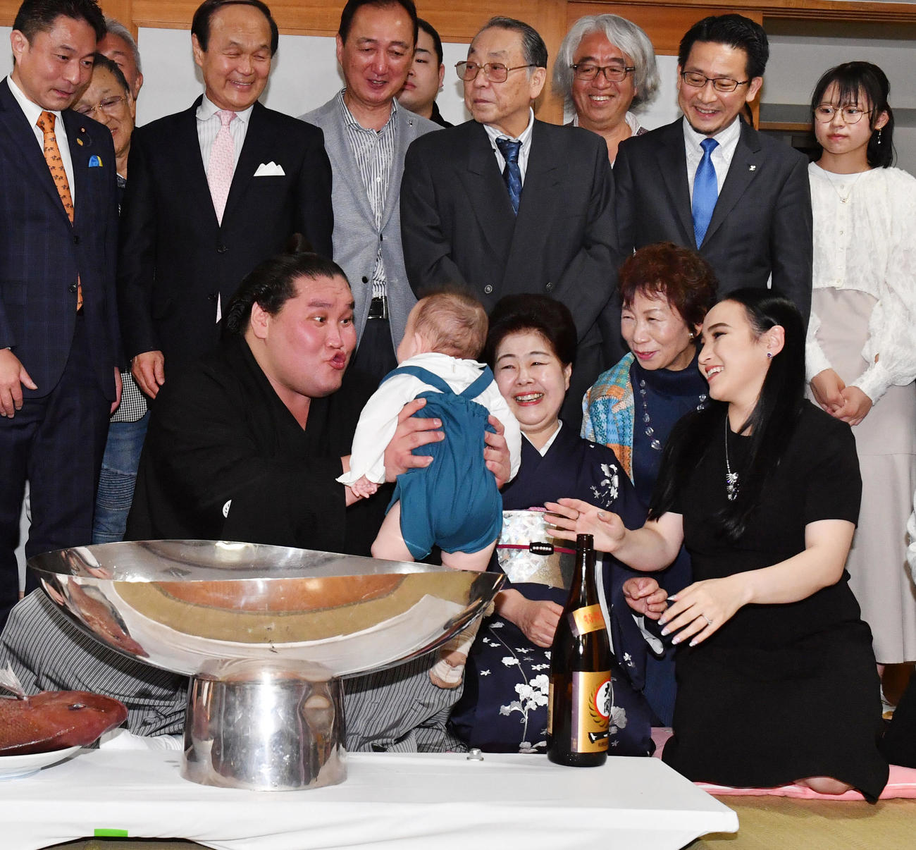 夏場所千秋楽、伊勢ケ浜部屋での祝賀会でツェグメド・ドルジハンド夫人（右）から手渡された長男・テムジン君を笑顔で抱く照ノ富士。前列右から2人目はおかみさんの淳子夫人（2023年5月28日撮影）