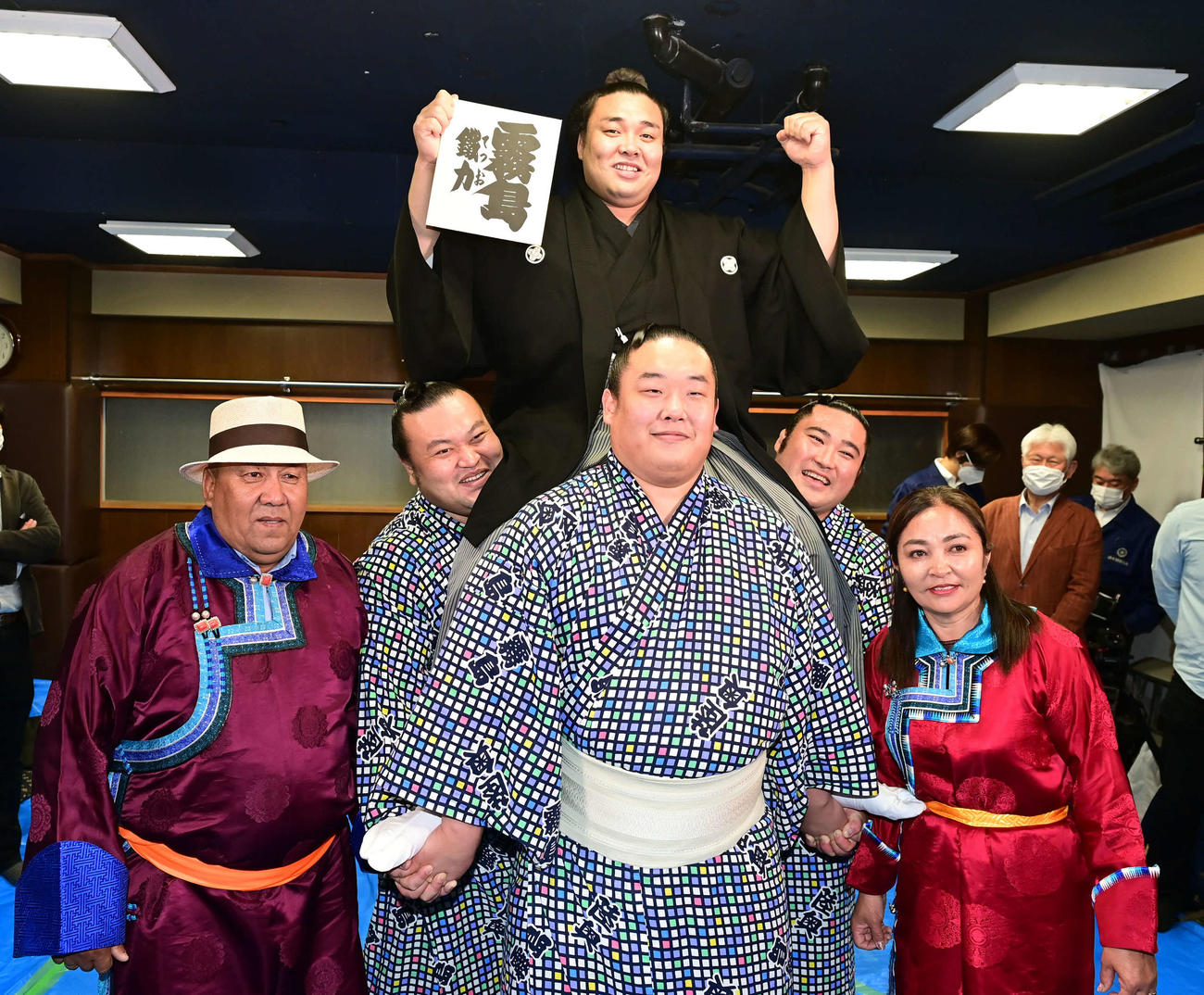 大関昇進伝達式を終えた霧馬山（上）は騎馬の上で新しいしこ名「霧島」と記された色紙を手にガッツポーズ。左から父ビャンブチュルンさん、勇輝、神谷、大日堂、母エンフゲレルさん（撮影・小沢裕）