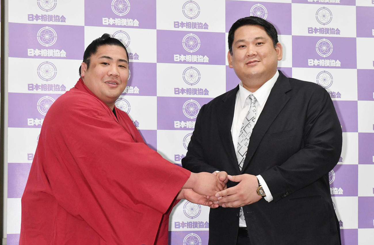 新十両昇進会見に臨んだ勇磨（左）は師匠の阿武松親方と握手する