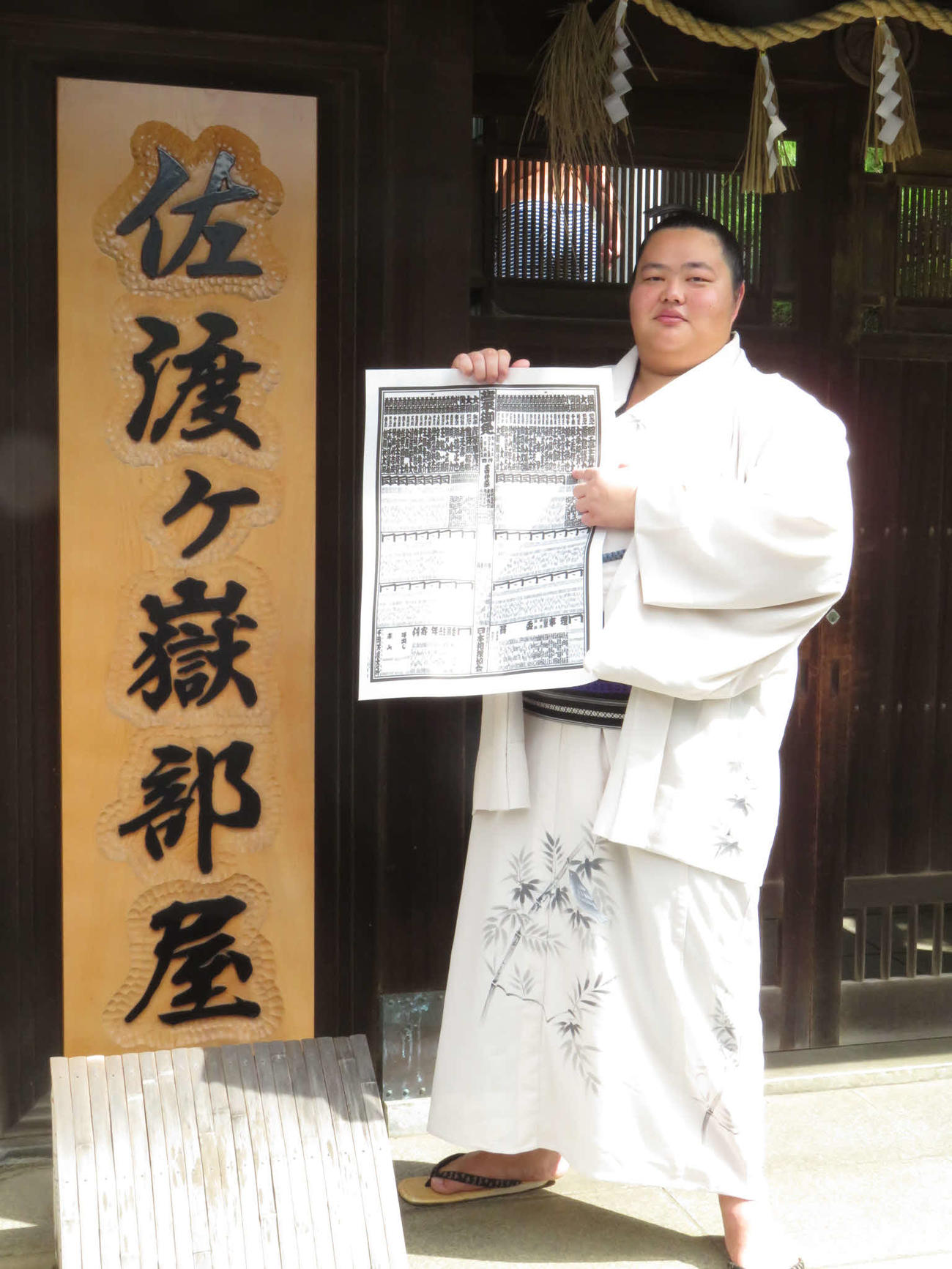 部屋の看板の前で、番付の自身のしこ名を指さしてほほ笑む琴ノ若