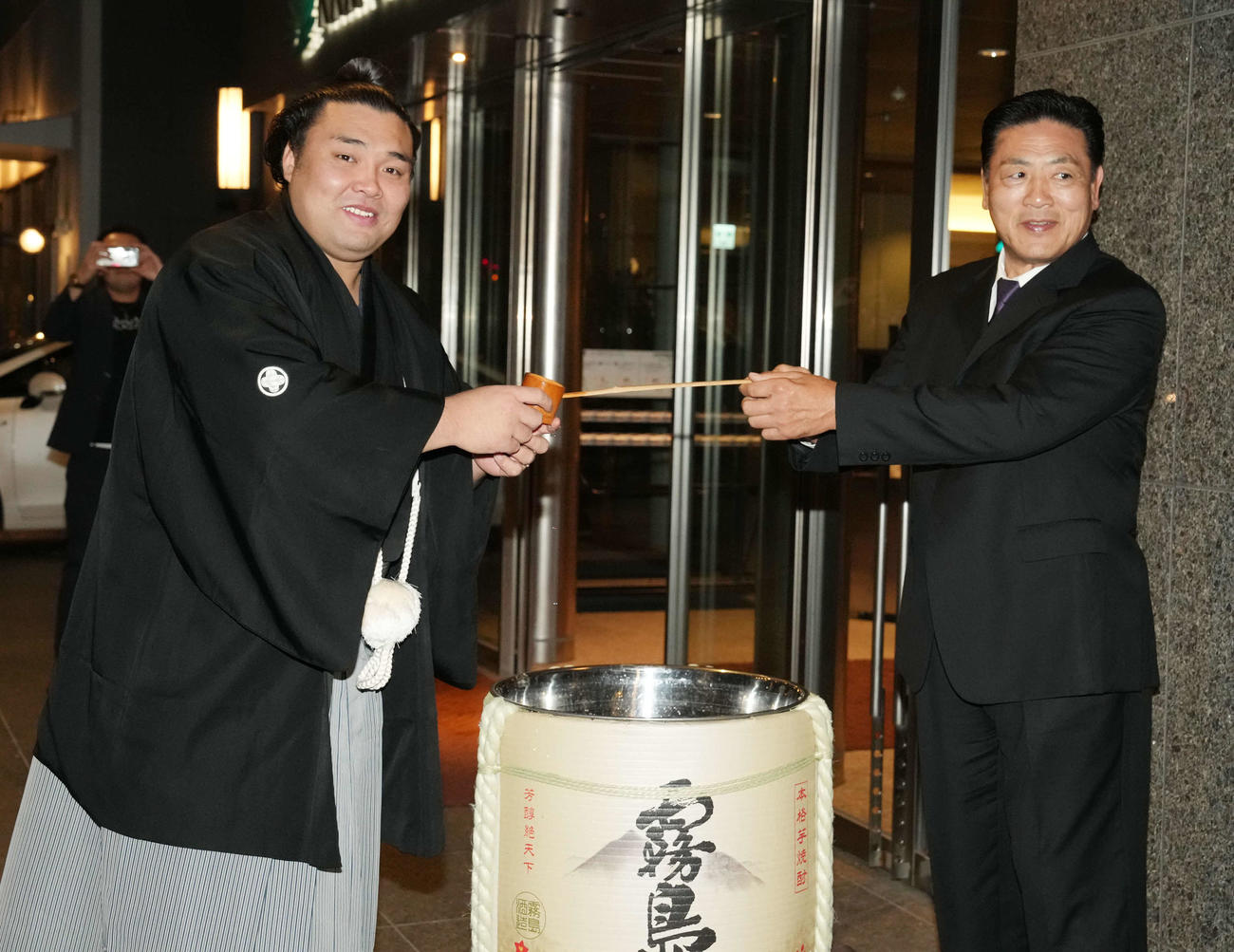 千秋楽パーティーが行われたホテルの入口で師匠の陸奥親方（右）から水付けを受ける霧島（撮影・小沢裕）