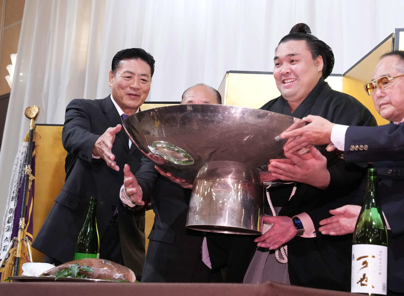 千秋楽パーティーで後援会関係者といっしょにお酒をそそがれた大杯を持ち上げる霧島。左端は師匠の陸奥親方（撮影・小沢裕）
