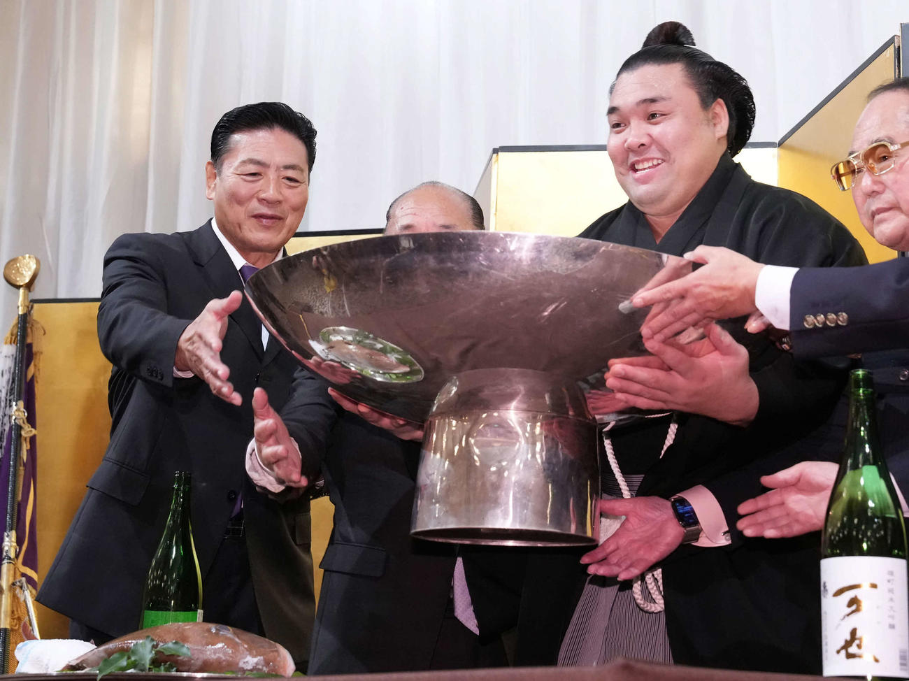 千秋楽パーティーで後援会関係者と一緒にお酒を注がれた大杯を持ち上げる霧島。左端は師匠の陸奥親方（撮影・小沢裕）