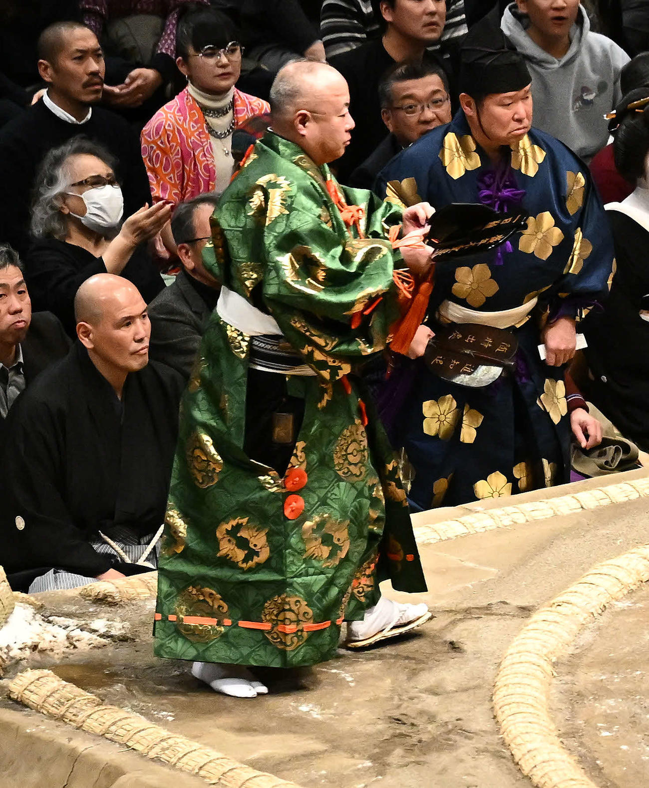 霧島と北勝富士の取り組みで転倒し落ちた烏帽子（えぼし）を手に立ち上がる行司木村容堂（手前）。後方は立ち上がる木村庄之助（撮影・滝沢徹郎）