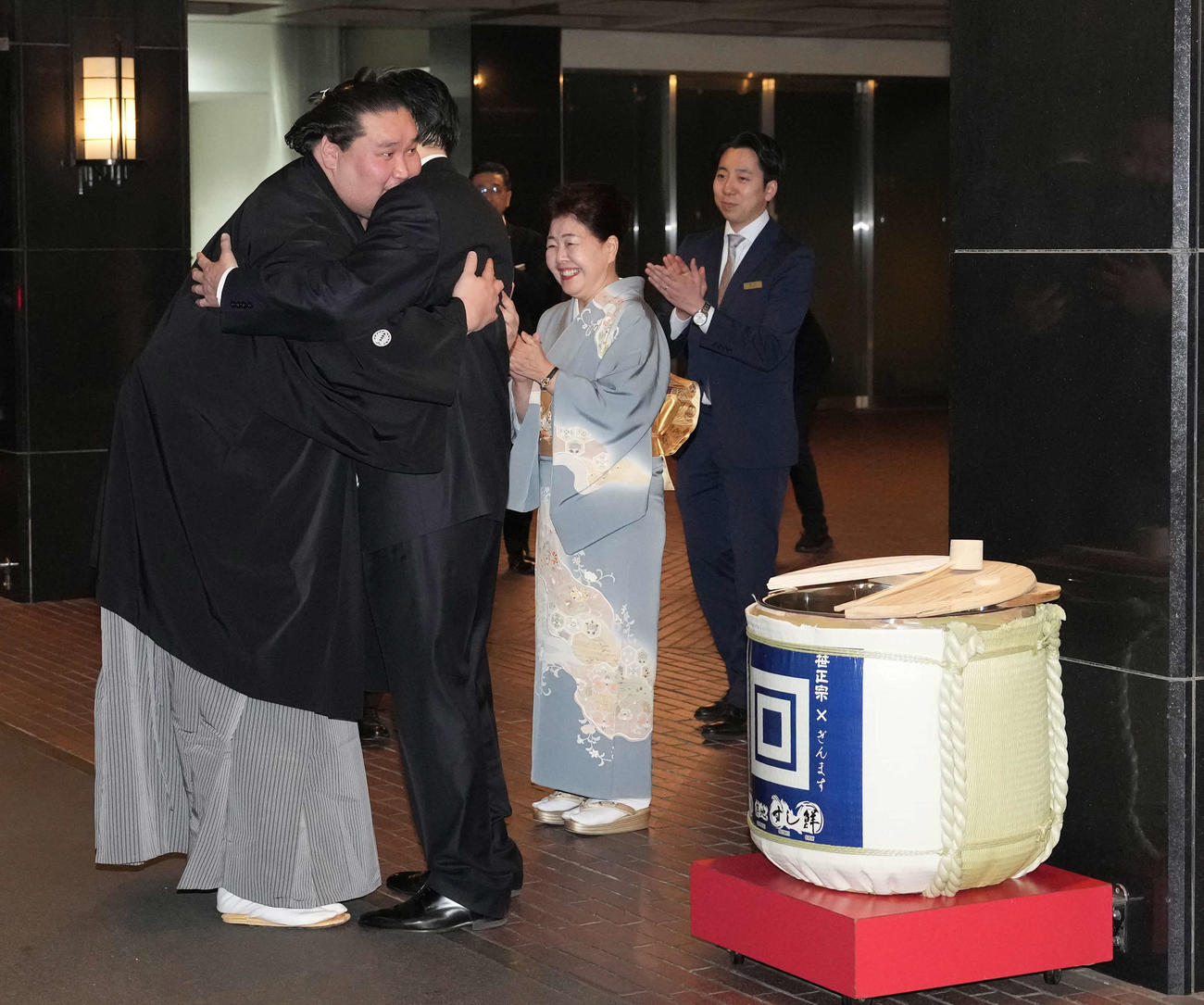 打ち上げパーティー会場のホテル前で師匠の伊勢ケ浜親方と抱擁する照ノ富士（左）。中央はおかみの淳子さん（撮影・小沢裕）