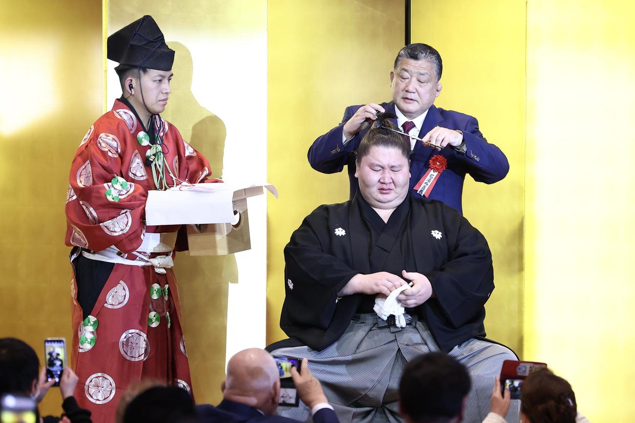 鳥取城北・石浦外喜義相撲部総監督（後方）に止めばさみを入れてもらう逸ノ城（撮影・河田真司）