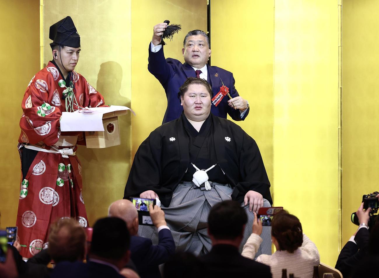鳥取城北・石浦相撲部総監督（奥）に止めばさみを入れてもらう逸ノ城（撮影・河田真司）