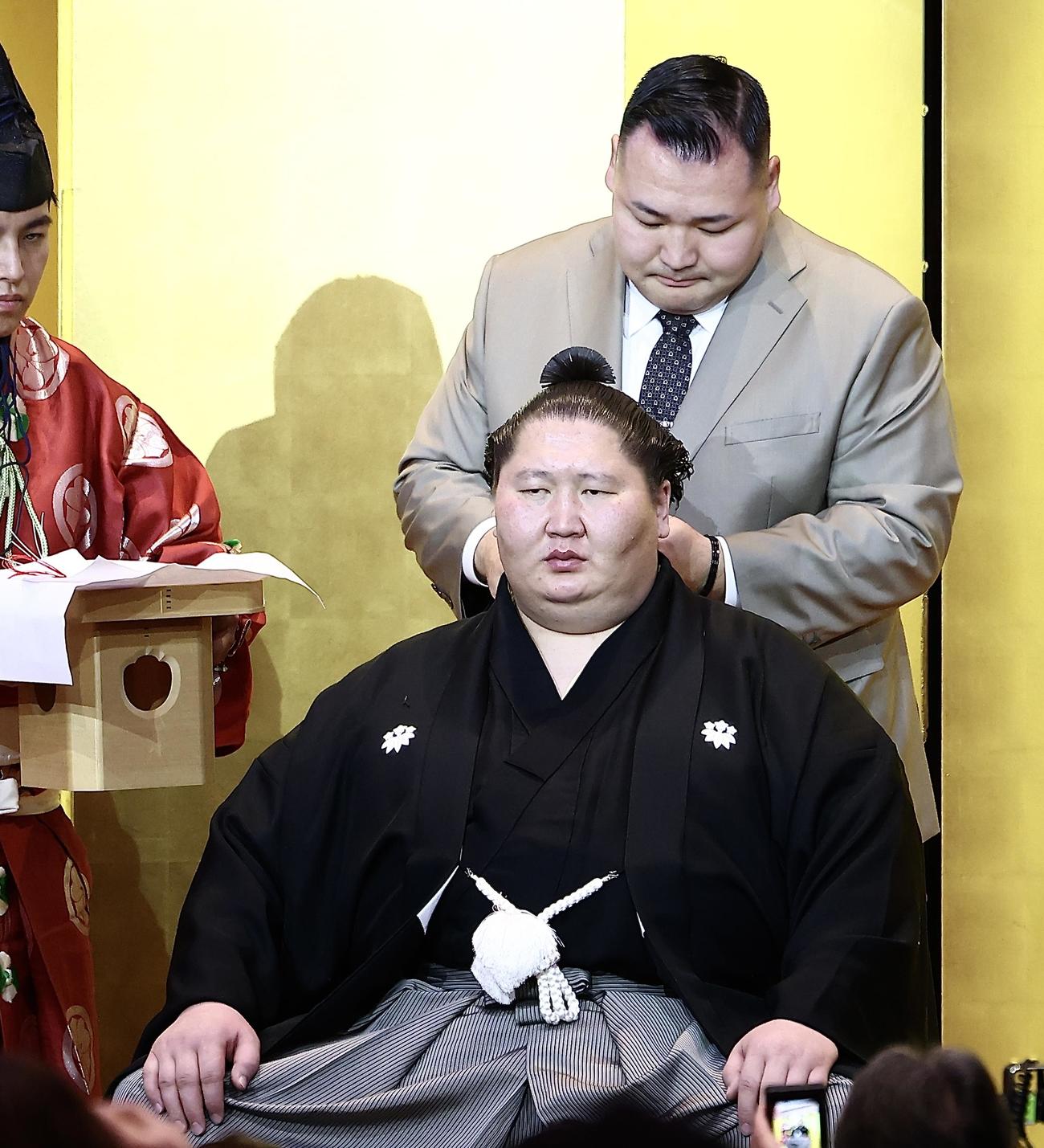 音羽山親方（奥）にはさみを入れてもらう逸ノ城（撮影・河田真司）
