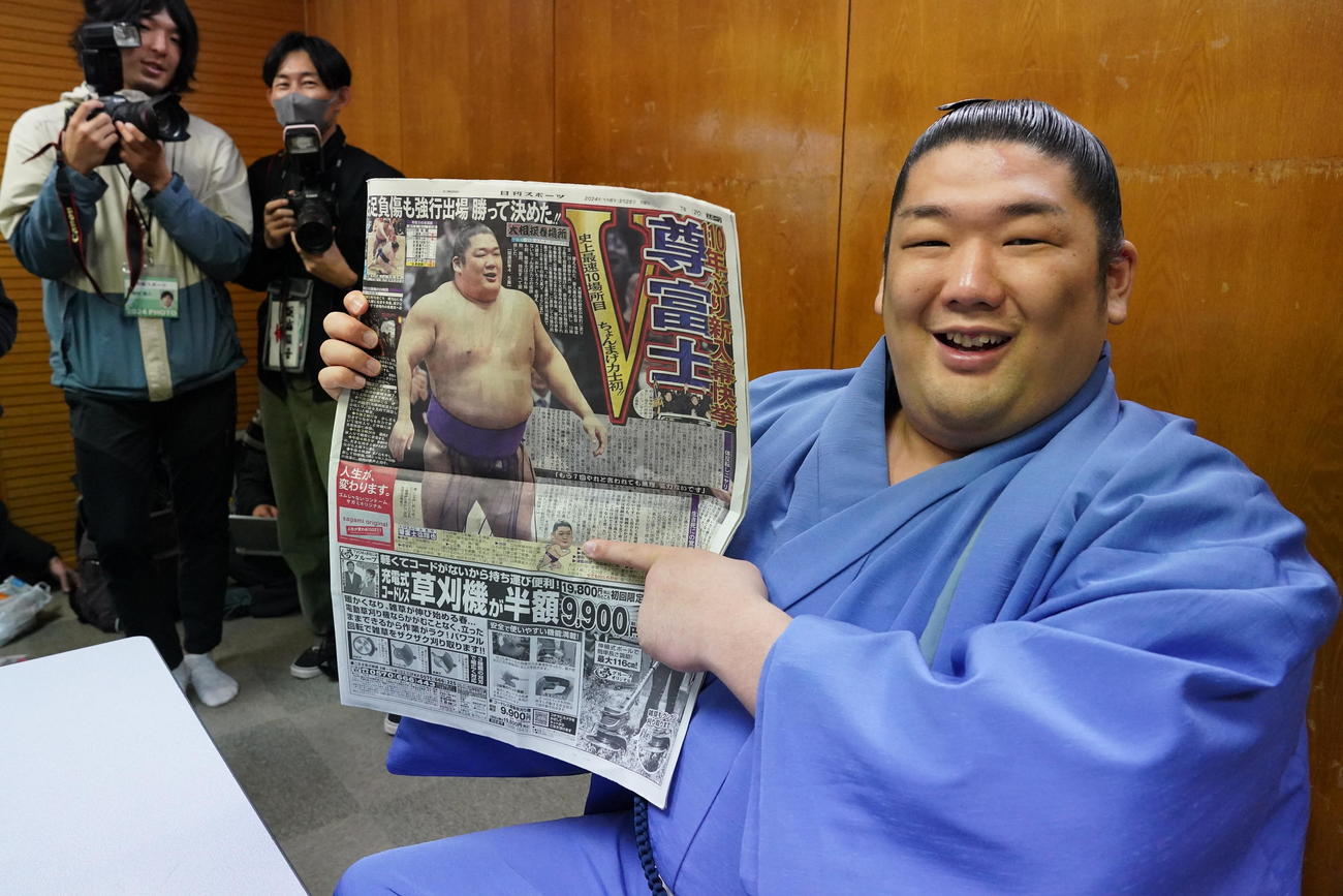 優勝一夜明け会見で本紙を手に笑顔を見せる尊富士（撮影・小沢裕）