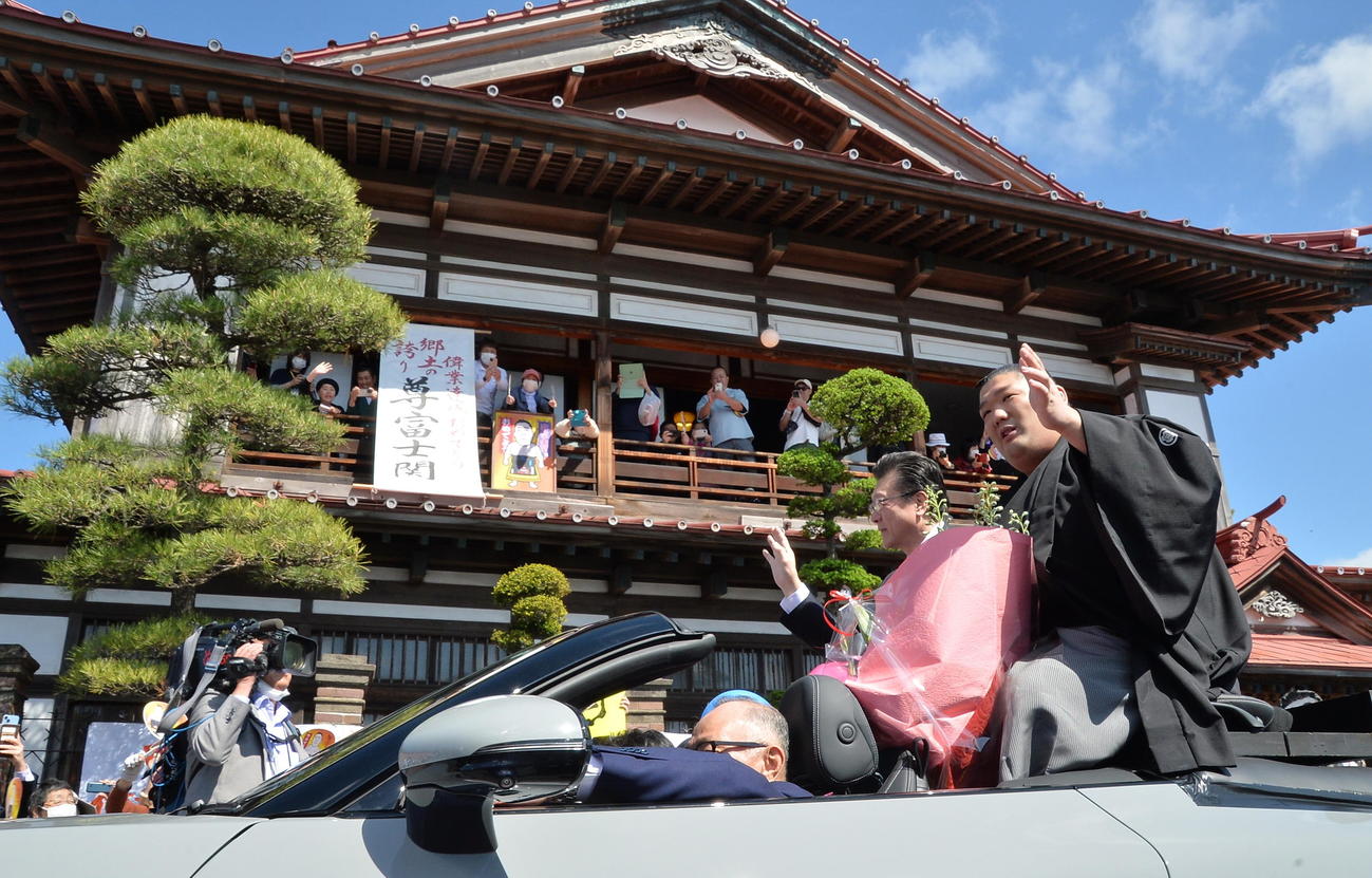 同郷の太宰治記念館「斜陽館」の前を通過し、ファンに手を振る尊富士。後方は伊勢ケ浜親方（撮影・濱本神威）