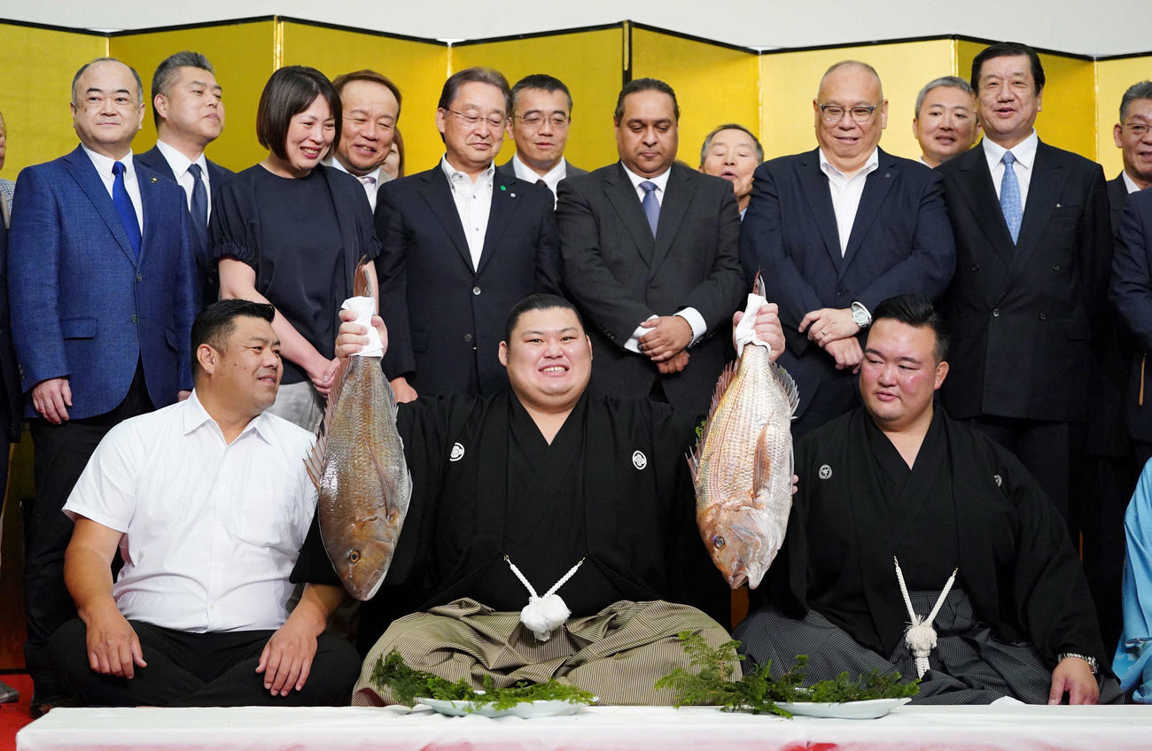 初優勝を飾った大の里（中央）は両手にお祝いの鯛を掲げる。右は師匠の二所ノ関親方、左は父知幸さん、後列左から4人目は母朋子さん（撮影・小沢裕）