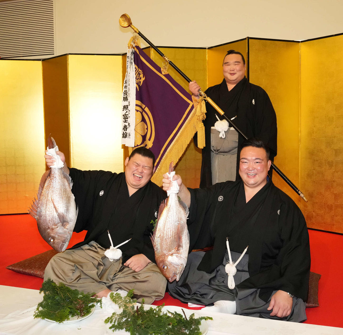 初優勝を飾った大の里（左）は師匠の二所ノ関親方とお祝いの鯛を掲げる。後方は白熊（撮影・小沢裕）