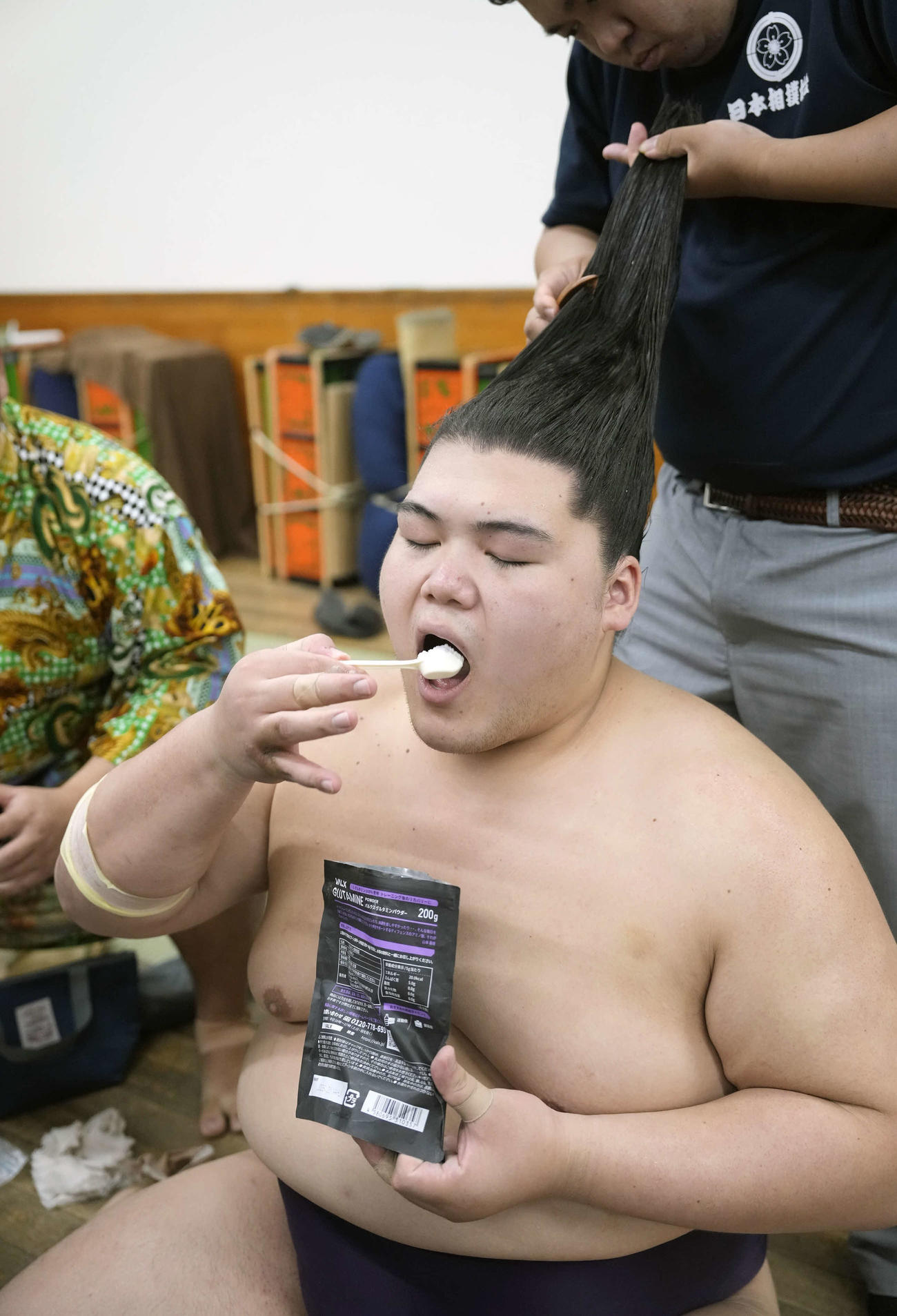 支度部屋で髪を整えながら栄養補助食品を口にする王鵬