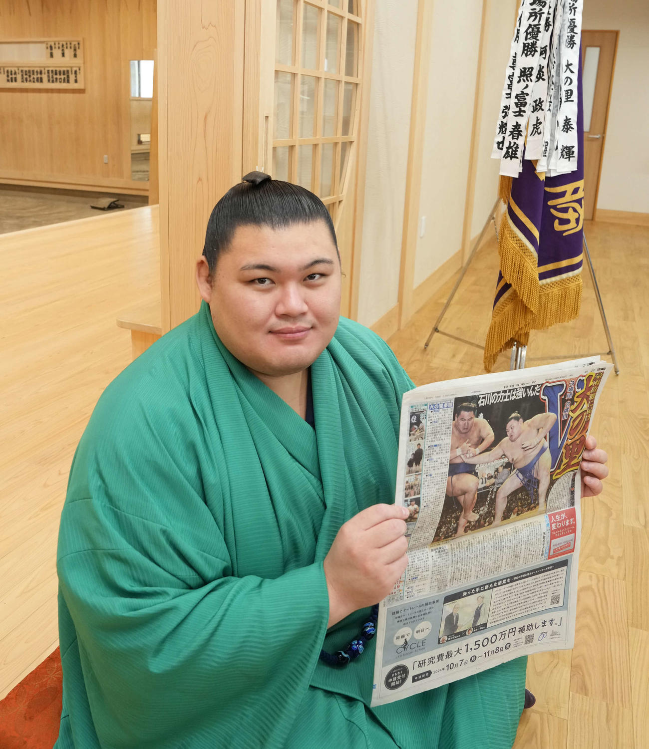 大相撲秋場所の優勝一夜明け会見で優勝を報じる本紙を手に笑顔を見せる大の里（撮影・小沢裕）