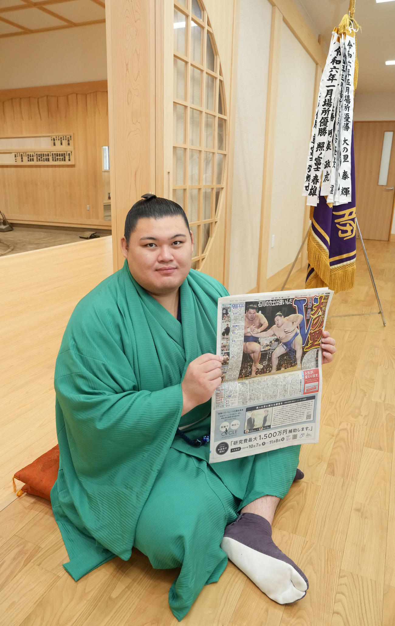 大相撲秋場所の優勝一夜明け会見で優勝を報じる本紙を手に笑顔を見せる大の里（撮影・小沢裕）