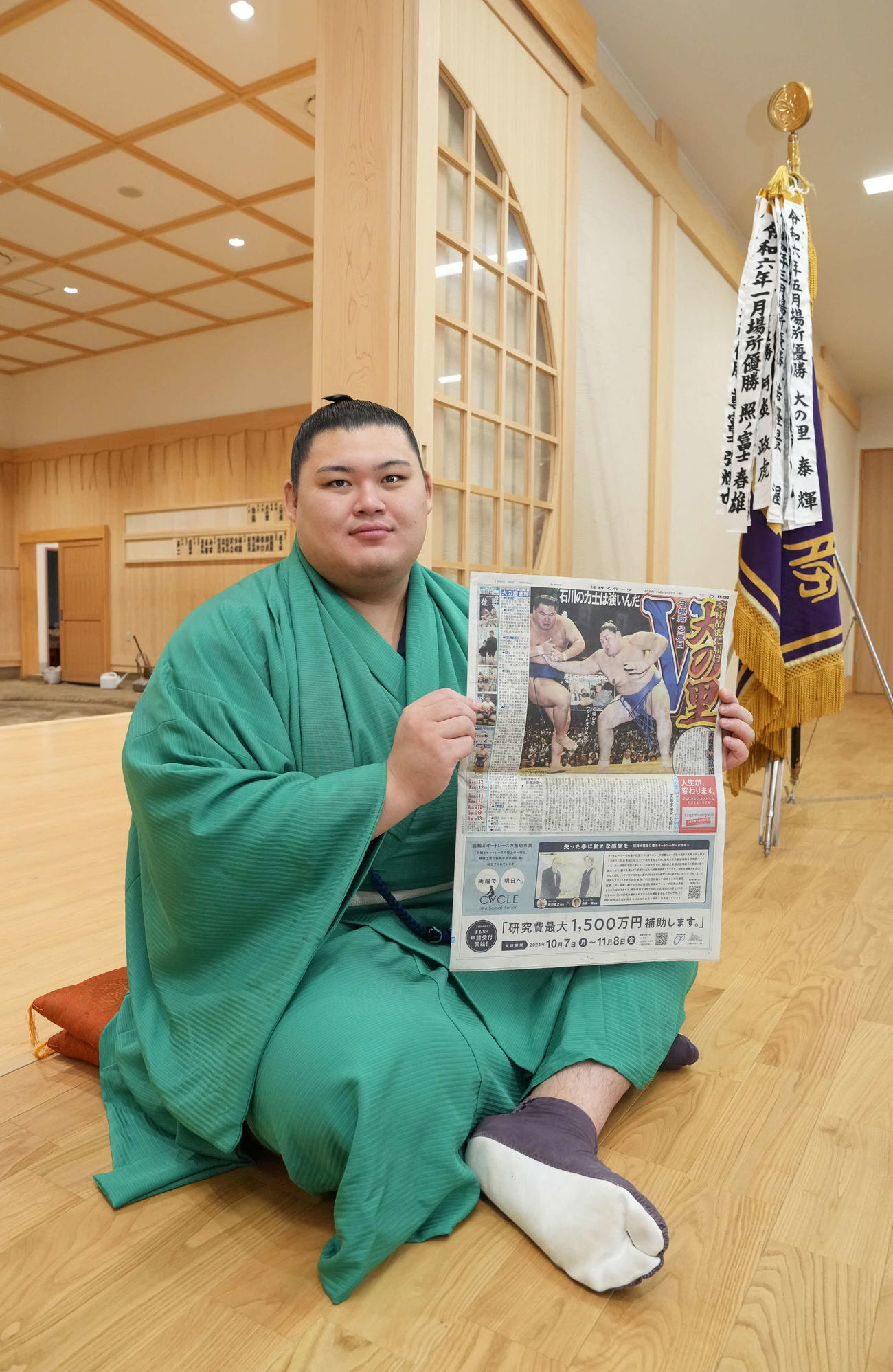 大相撲秋場所の優勝一夜明け会見で優勝を報じる本紙を手に笑顔を見せる大の里（撮影・小沢裕）