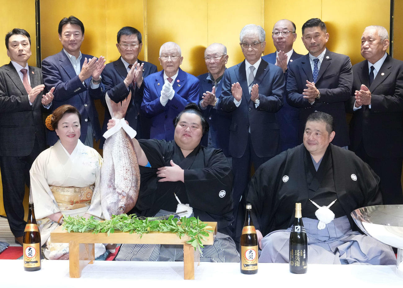 初優勝を飾った琴桜（中央）は千秋楽パーティー会場で関係者の祝福を受けながらお祝いの鯛を持ち上げる。右は父であり師匠の佐渡ケ嶽親方、左は母でおかみの真千子さん（撮影・小沢裕）