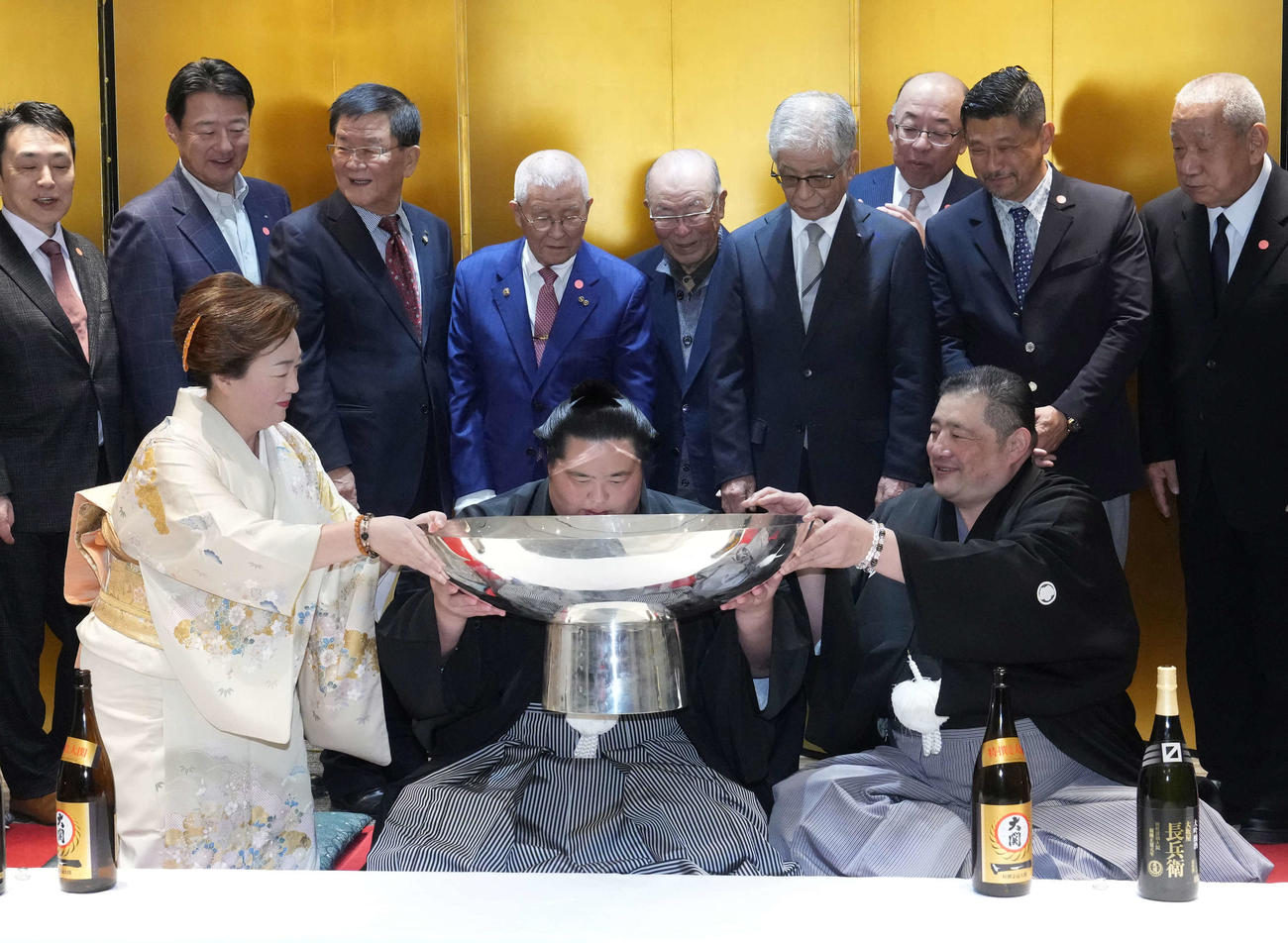 初優勝を飾った琴桜（中央）は千秋楽パーティー会場で父であり師匠の佐渡ケ嶽親方（右）、母でおかみの真千子さん（左）の力を借りながらお祝いのお酒がそそがれた銀杯に口を付ける（撮影・小沢裕）