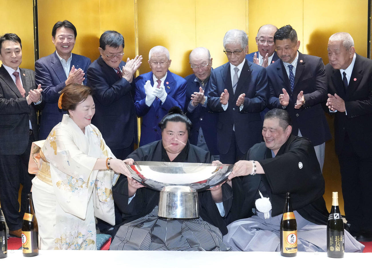 初優勝を飾った琴桜（中央）は千秋楽パーティー会場で父であり師匠の佐渡ケ嶽親方（右）、母でおかみの真千子さん（左）の力を借りながらお祝いのお酒がそそがれた銀杯に口を付ける（撮影・小沢裕）