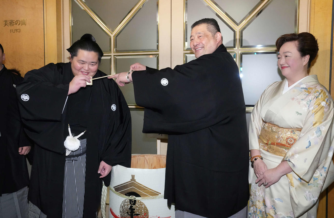 初優勝を飾った琴桜（左）は千秋楽パーティー会場で父である師匠の佐渡ケ嶽親方から水を付けてもらう。右は母でおかみの真千子さん（撮影・小沢裕）