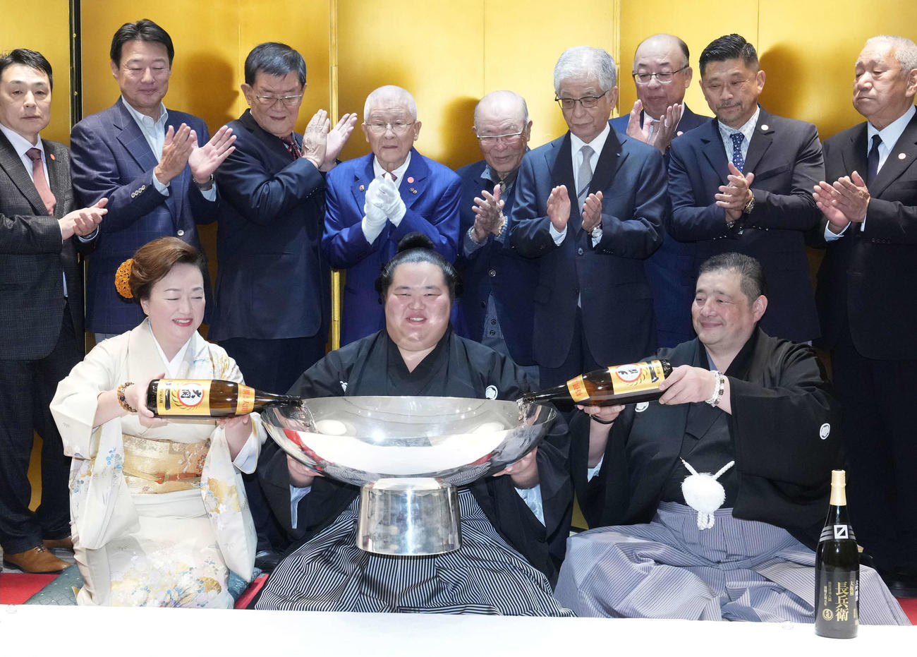 初優勝を飾った琴桜（中央）は父であり師匠の佐渡ケ嶽親方（右）、母でおかみの真千子さん（左）から銀杯にお酒をそそがれて笑顔を見せる（2024年11月24日撮影）