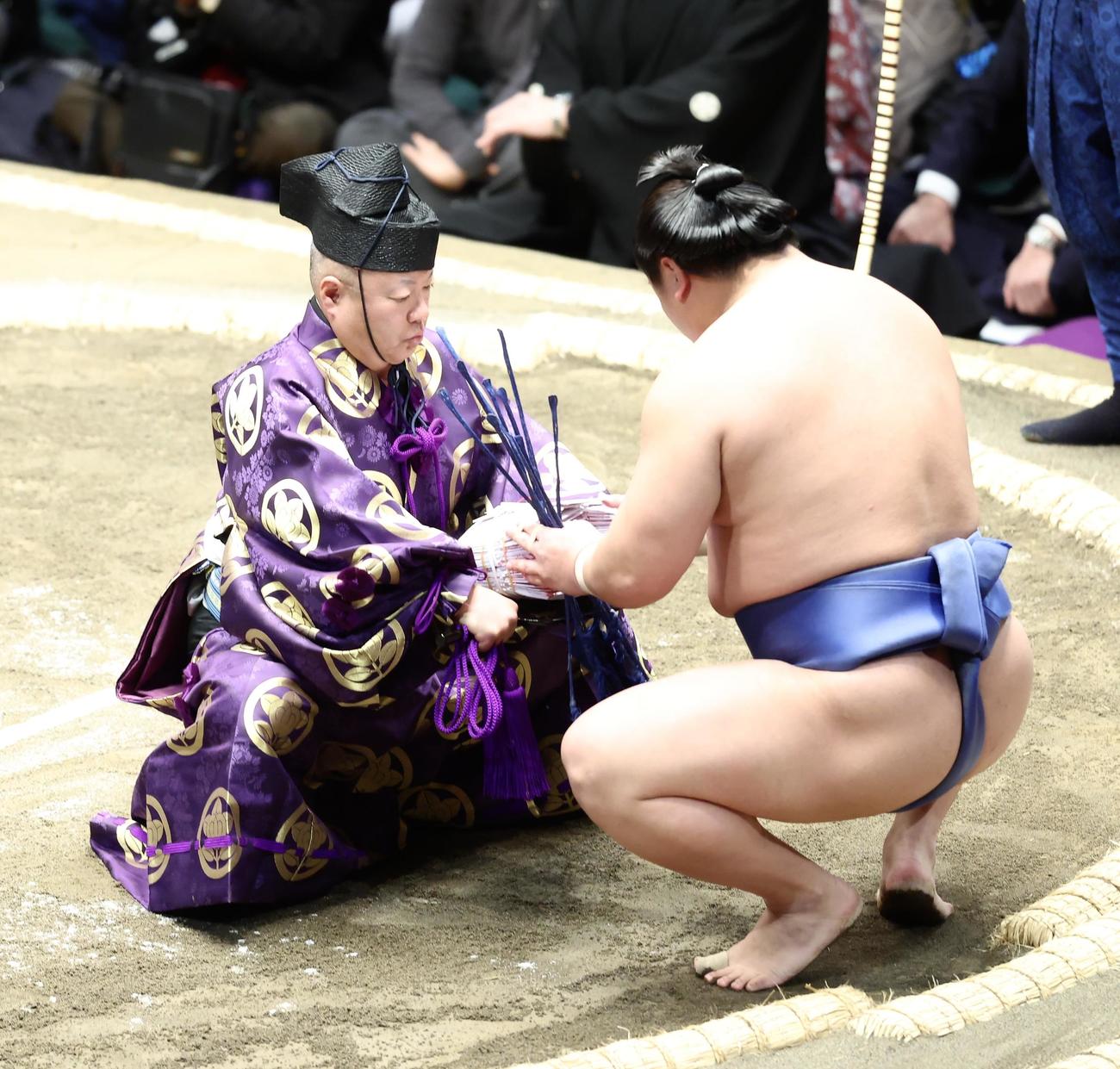 照ノ富士を肩すかしで破り、木村庄之助（左）から懸賞金の束を受け取る若隆景（撮影・河田真司）