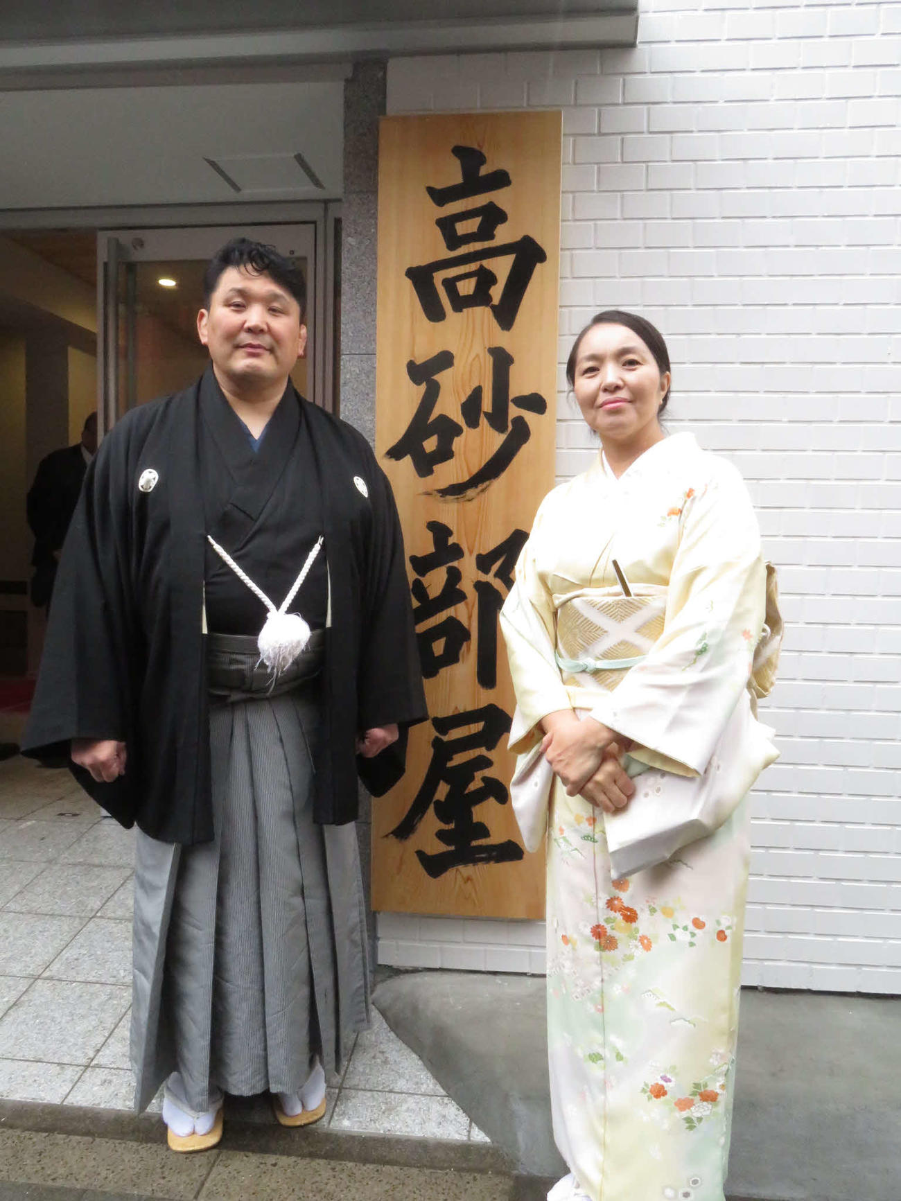 部屋開きの各種行事を終え、看板の前で記念撮影に納まる高砂親方（左）とデルゲレツェツェゲ夫人