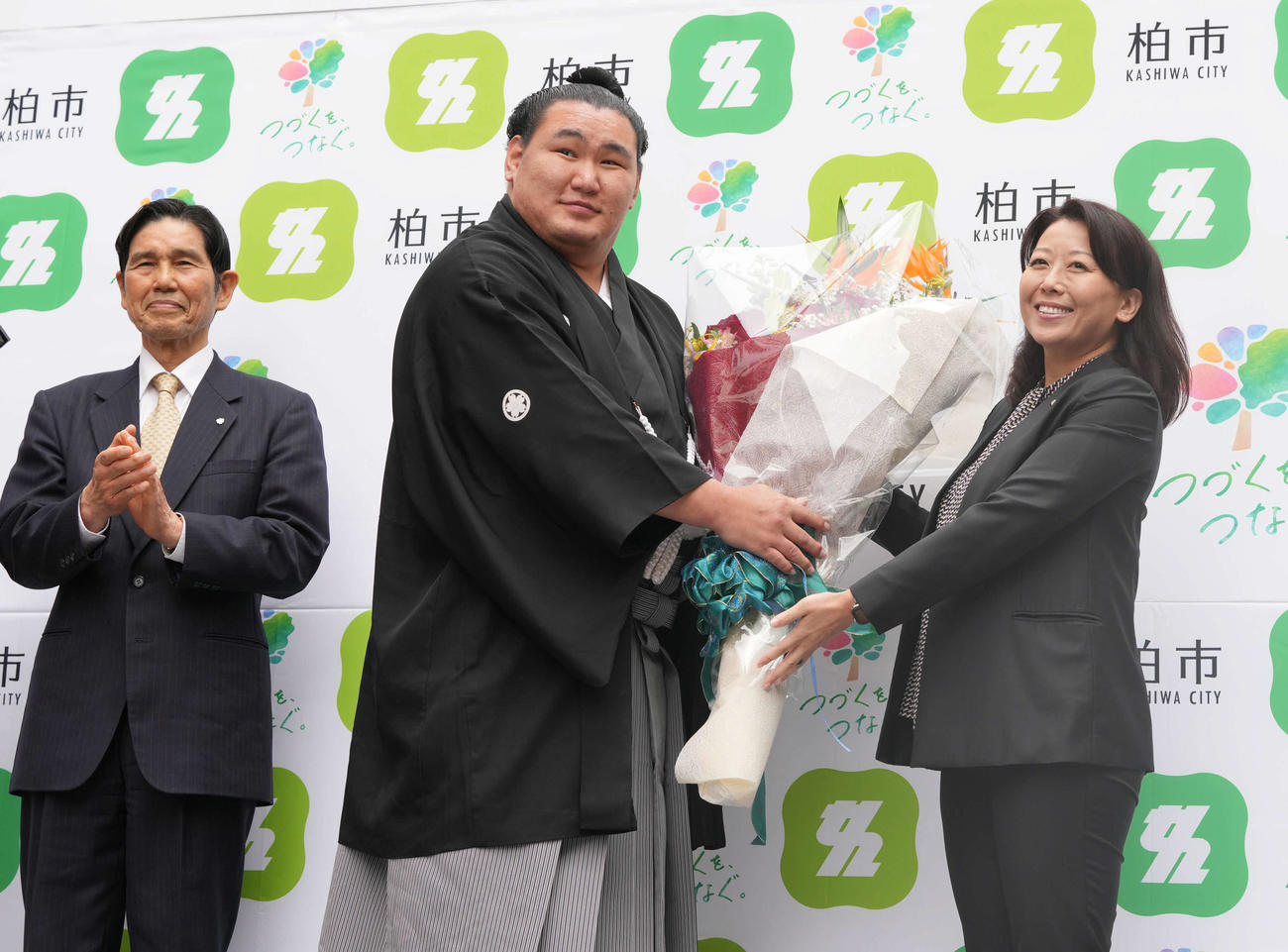 高校時代にゆかりのある千葉県柏市内で開催された横綱昇進祝賀パレードを終えた豊昇龍は柏市の太田市長（右）から花束贈呈を受ける。左は日体柏高の氷海校長（撮影・小沢裕）