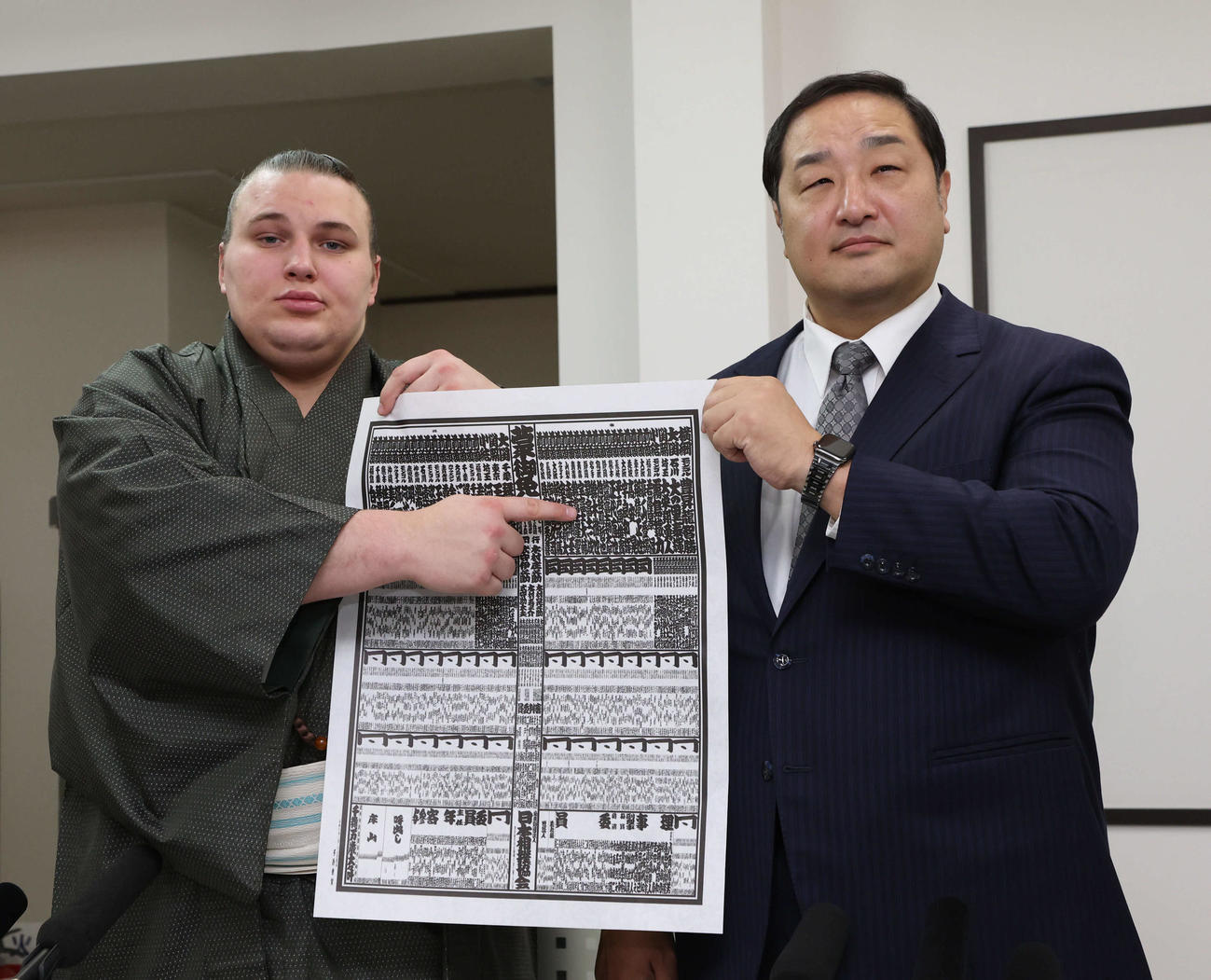 新入幕の安青錦（左）は師匠の安治川親方（元関脇安美錦）とともに新しい番付を指さす（撮影・西尾就之）