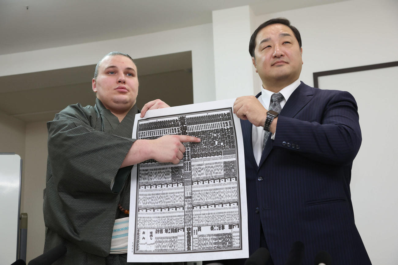 新入幕の安青錦（左）は師匠の安治川親方（元関脇安美錦）とともに新しい番付を指さす（撮影・西尾就之）